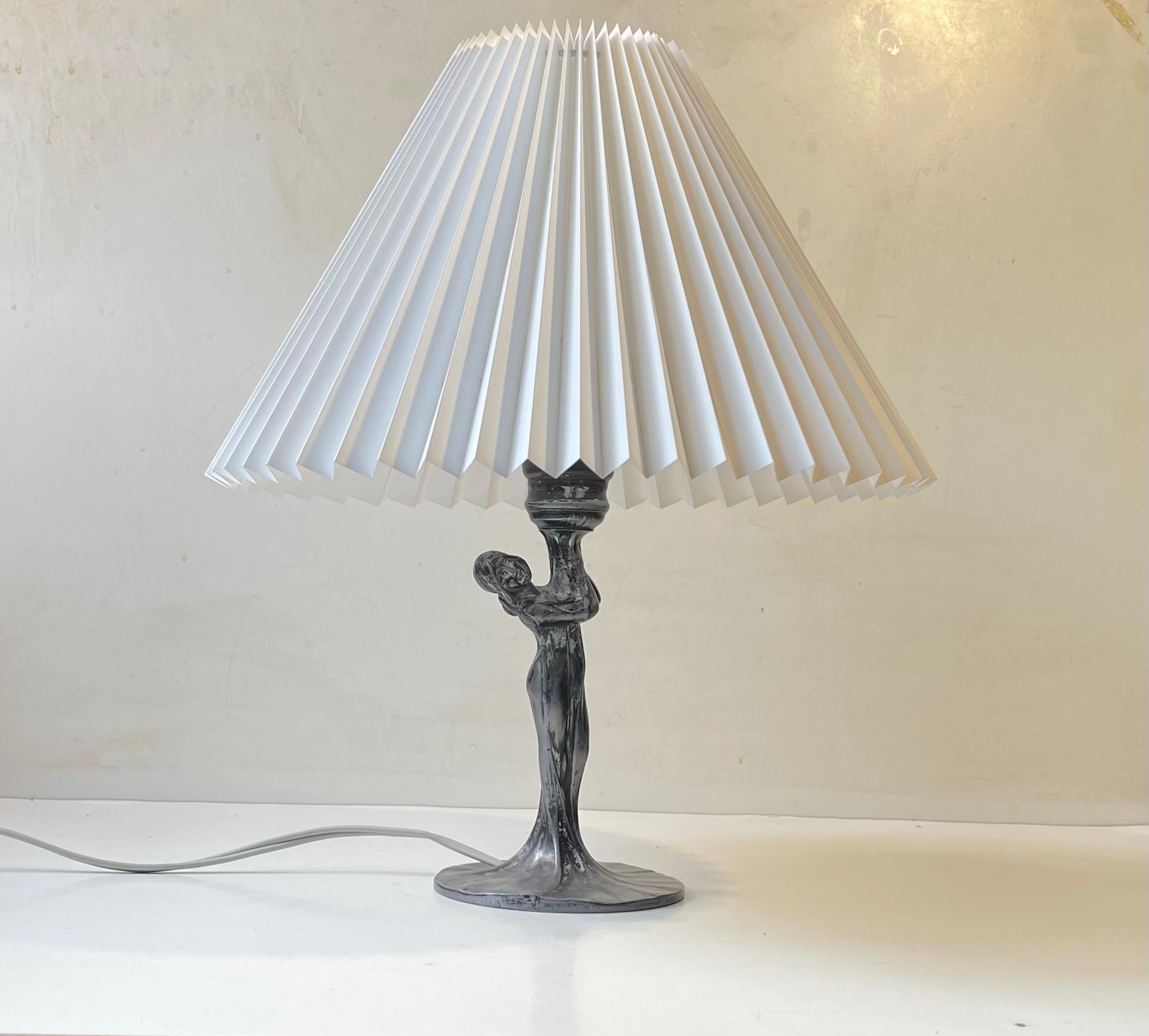 I the style of Max Le Verrier and Leonardine comes this stylized table lamp in patinated pewter. It depicts a woman whos dress floats down and creates the base. It was made in France circa 1920-40. It comes mounted with a new fluted white shade.