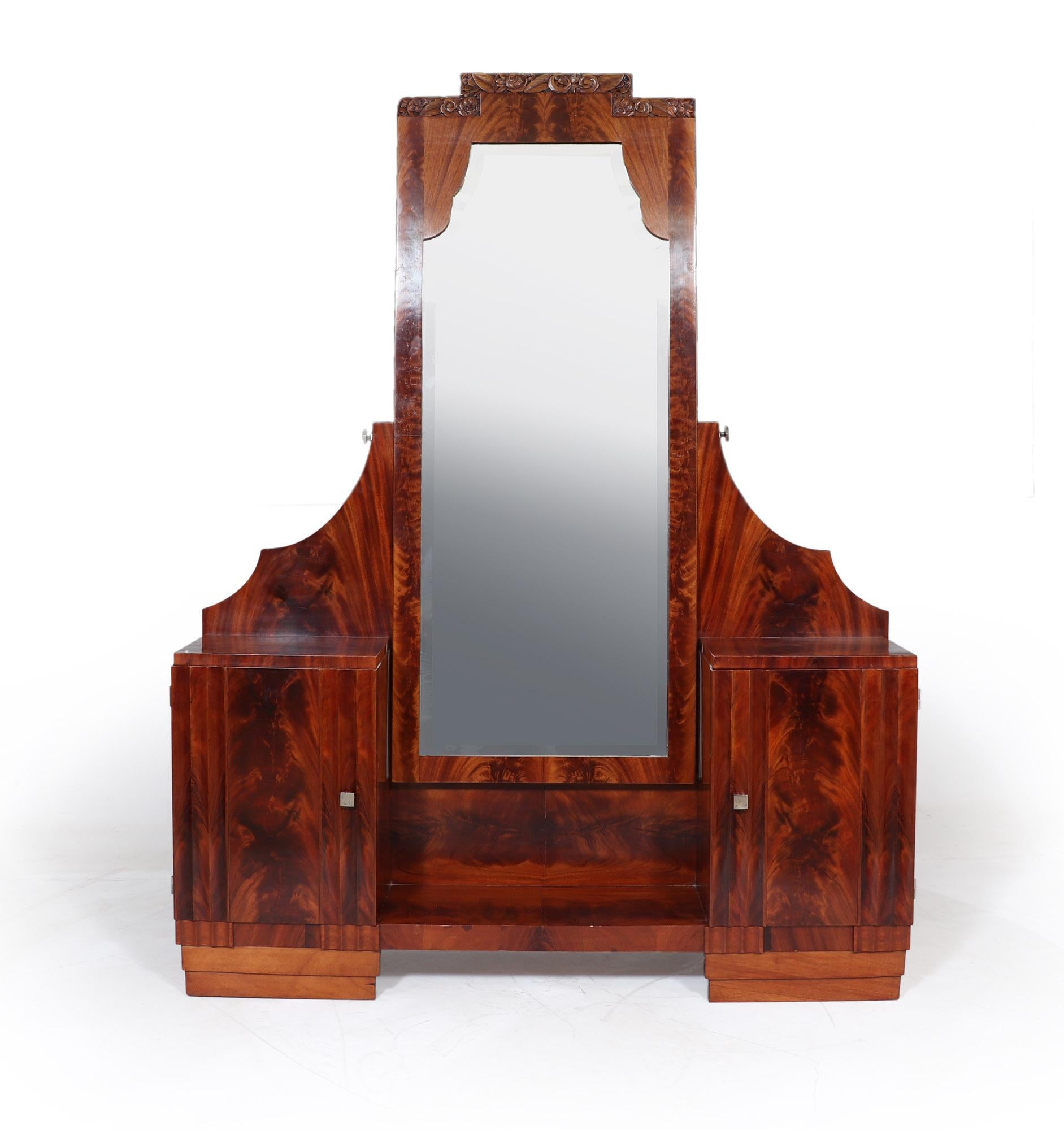 A French Art Deco dressing table in flame mahogany, with full length shaped top bevelled cheval mirror that is angle adjustable with silvered square knobs, two cabinets with single door and drawer behind the dressing table has been restored where