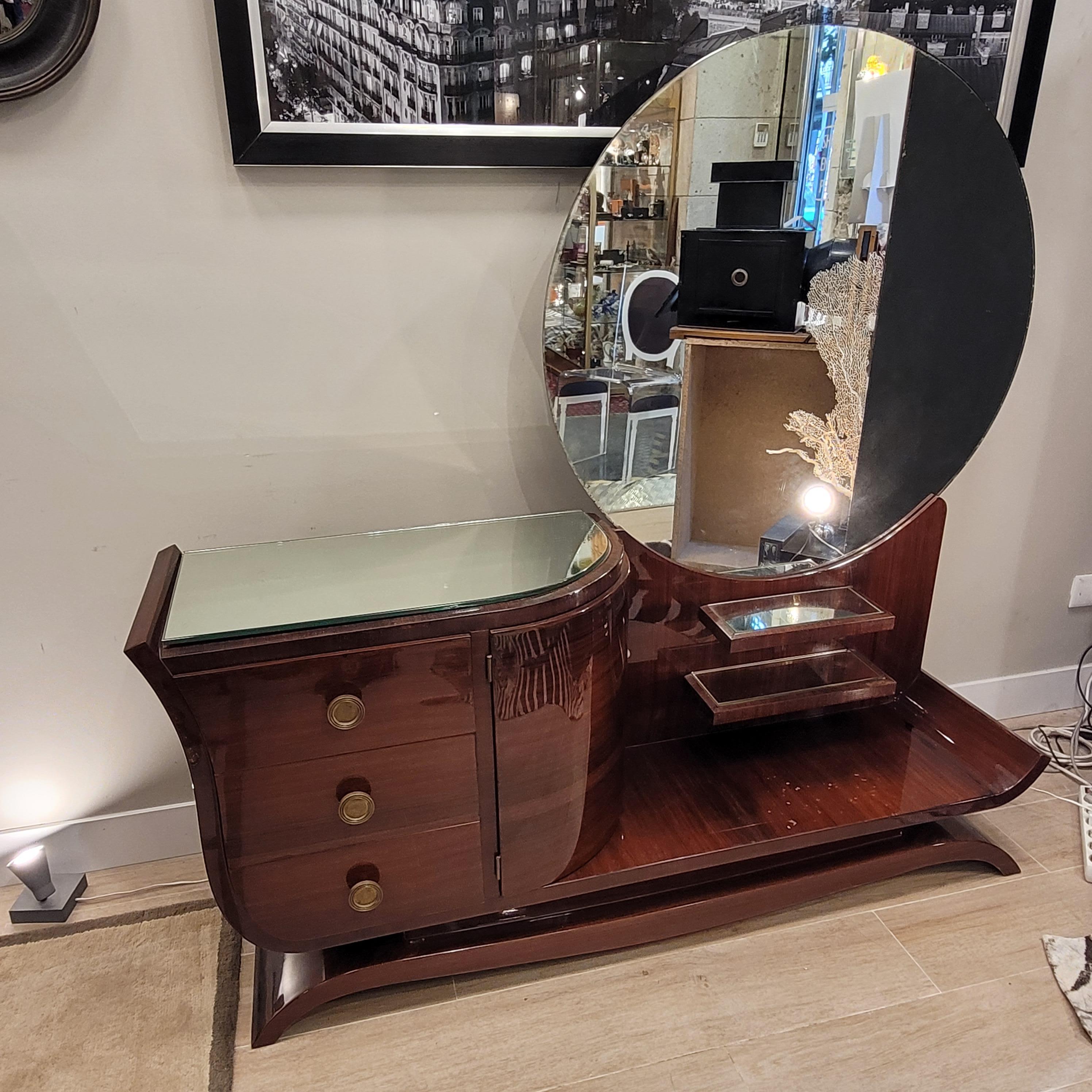 Exquisite Art Deco dressing table made around 1930 in mahogany wood. With elegant shapes, this dressing table is configured in two different parts, the furniture itself and the completely circular mirror. Its design is asymmetrical, playing with the