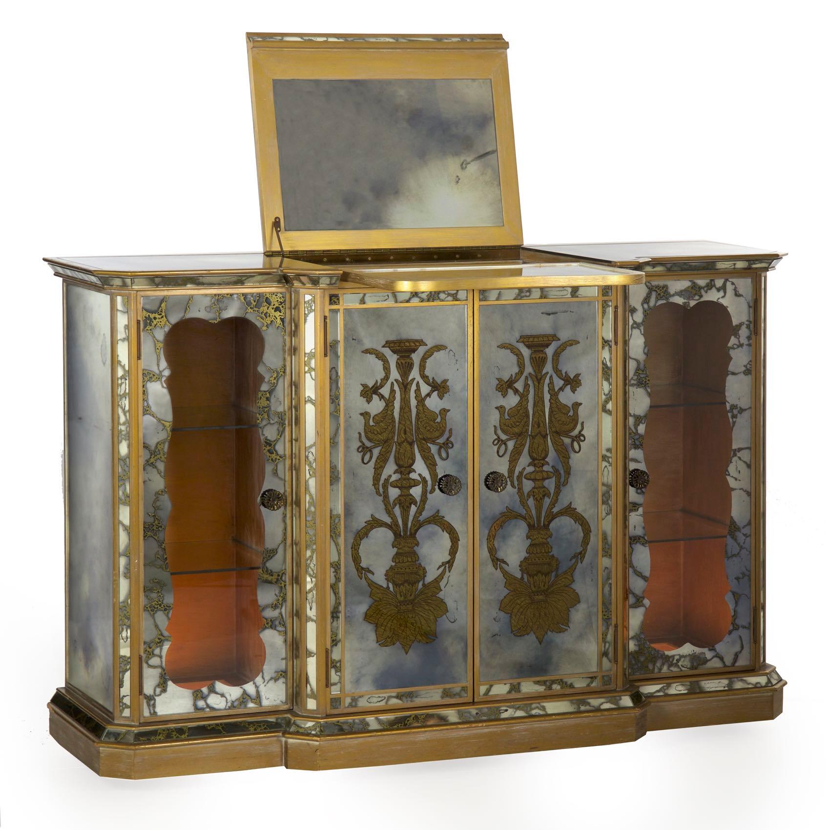 An unusual and interesting Art Deco bar serving console from the second quarter of the 20th century, the use of smoked mirrored glass is rather dramatic against the mellow white-washed gilding of the frame. The eglomisé decorating of the glass is