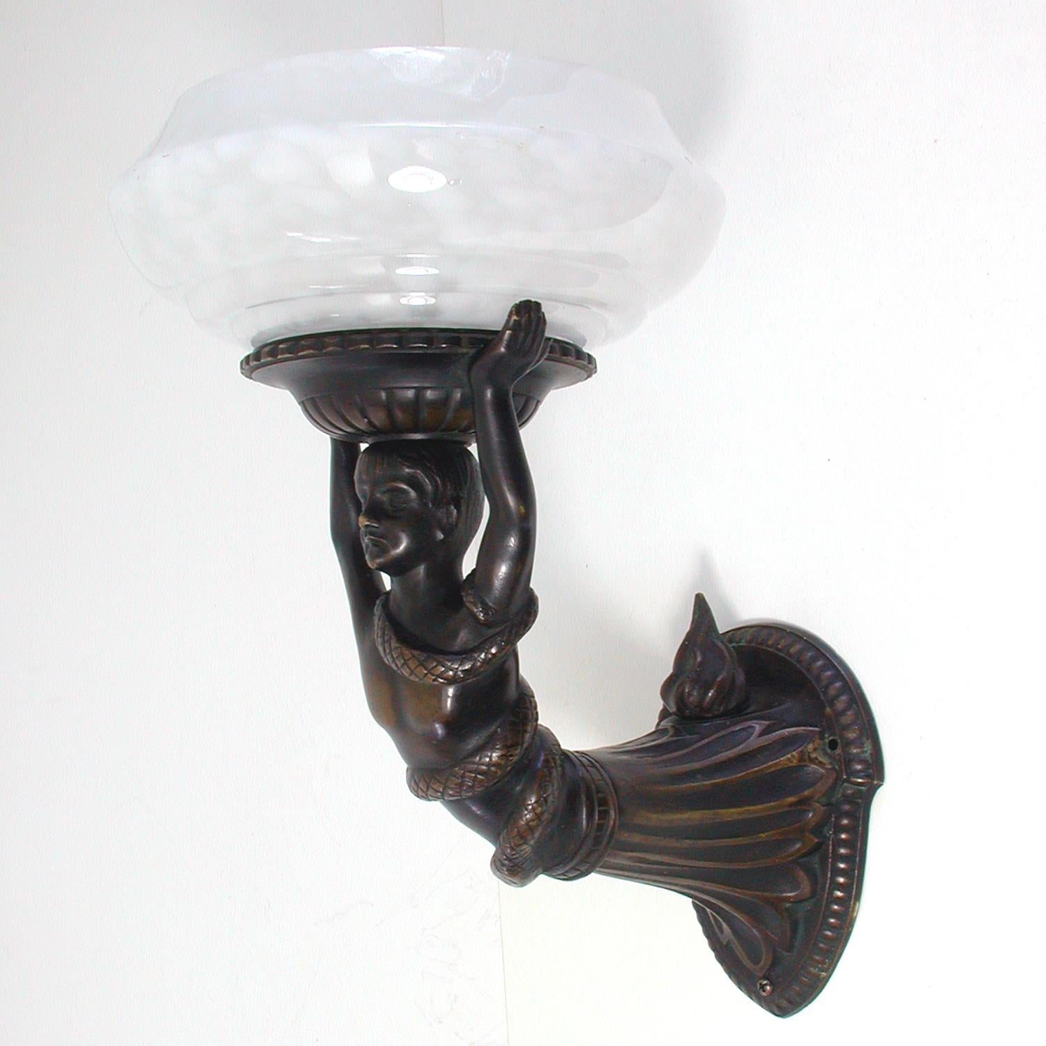 This unusual bronze wall light was designed and manufactured in France in the early 1920s. It features a lady with a snake winding around her body and her holding a mottled glass lamp shade above her head.

The lamp has got a French B22 socket and