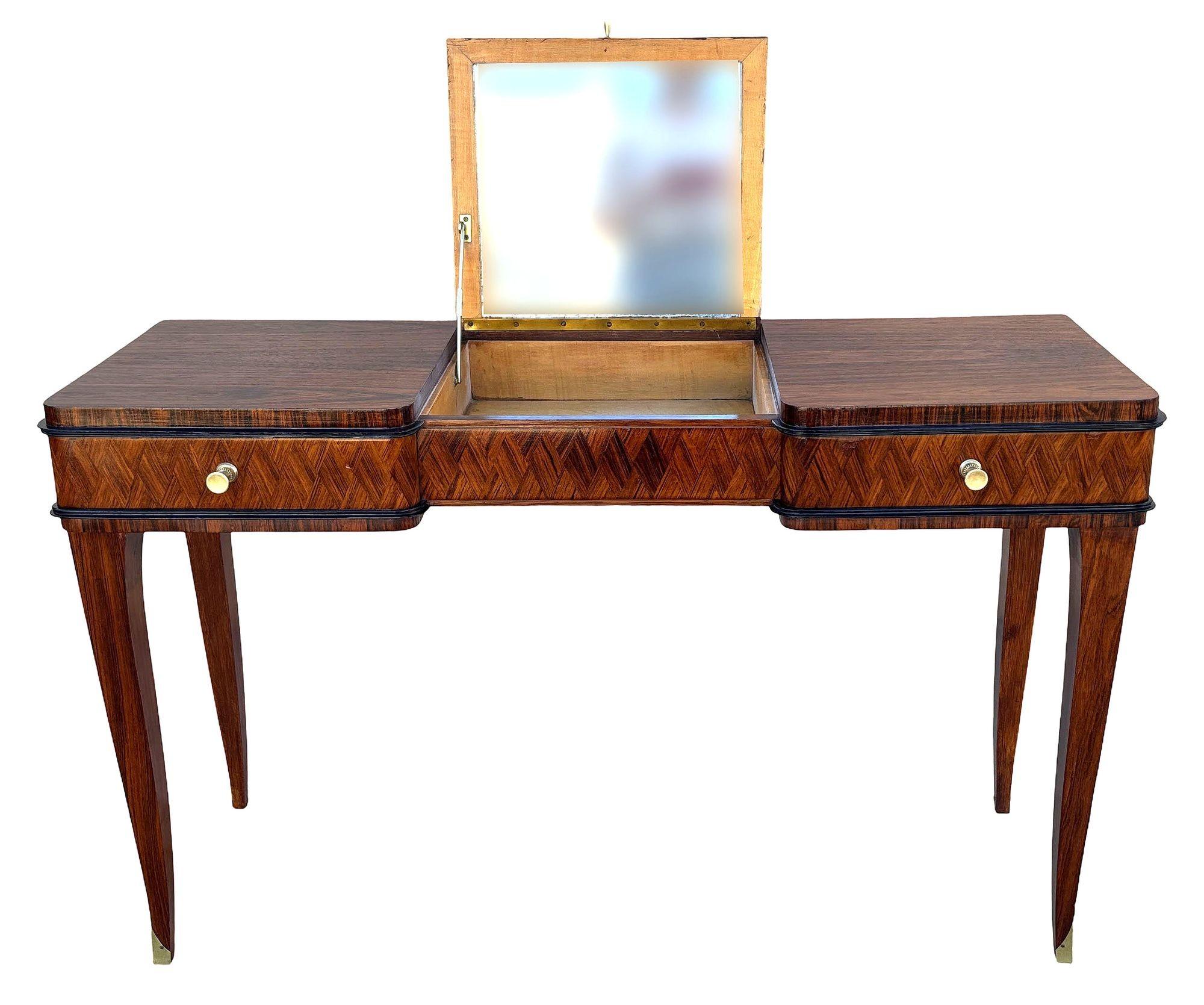 Elegante tocador francés Art Decó de palisandro de Madagascar y latón, con elegantes patas cónicas, pies rematados en latón y detalles geométricos de parquetería. El compartimento central se abre para mostrar un espejo empotrado, mientras que los