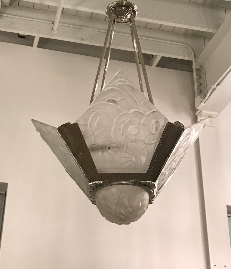 French Art Deco chandelier by famous artist Degué. Having four clear frosted glass panels and center globe with polished details and floral motif. Held by a polished nickel design frame. All the glass is signed 