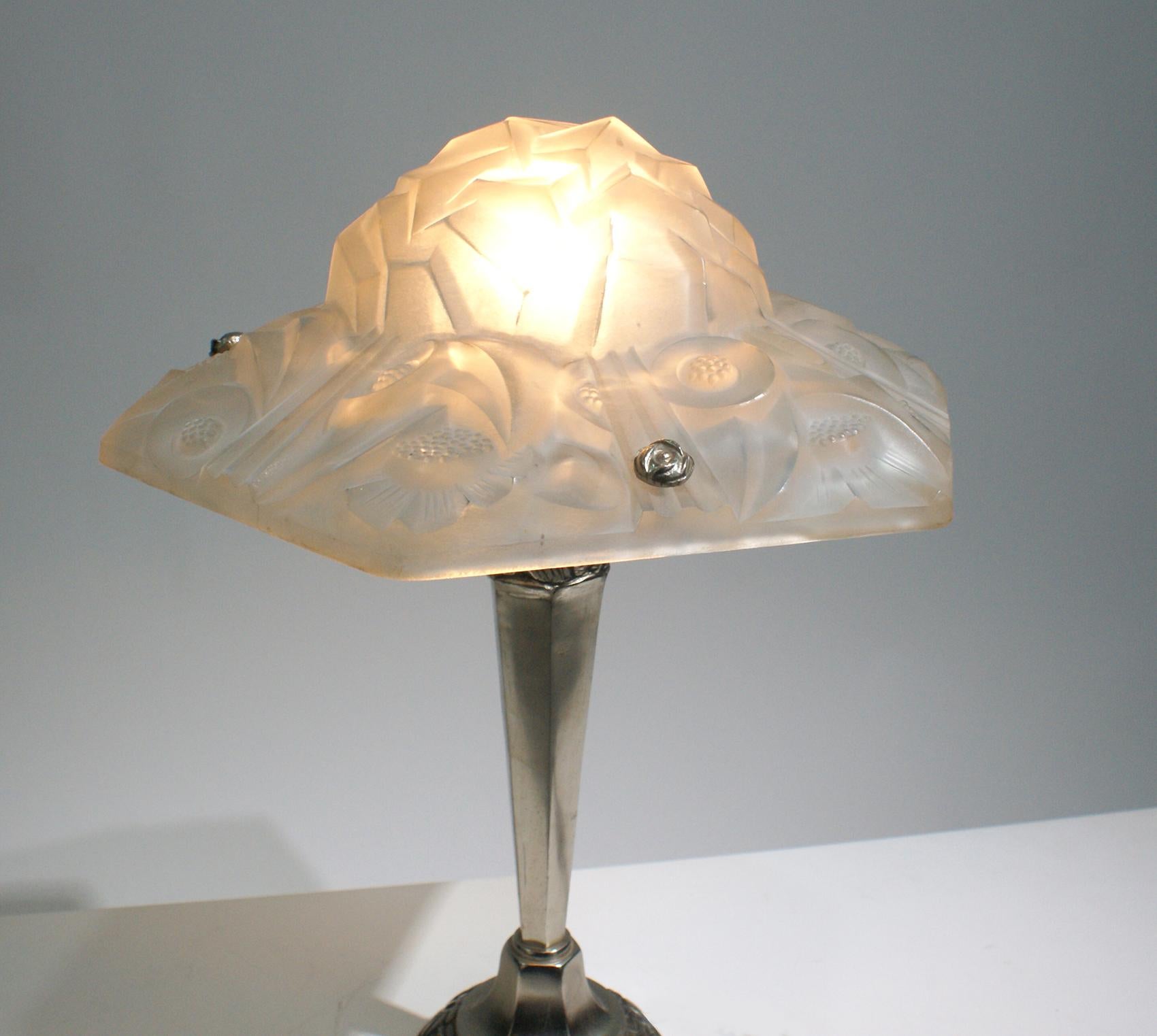 Stunning French Art Deco table lamp signed by “Degue”. Having frosted geometric and floral motif design in relief including “Degué” signature on the glass shade shaped like a hat. Resting on matching floral nickeled bronze column.
The table lamp