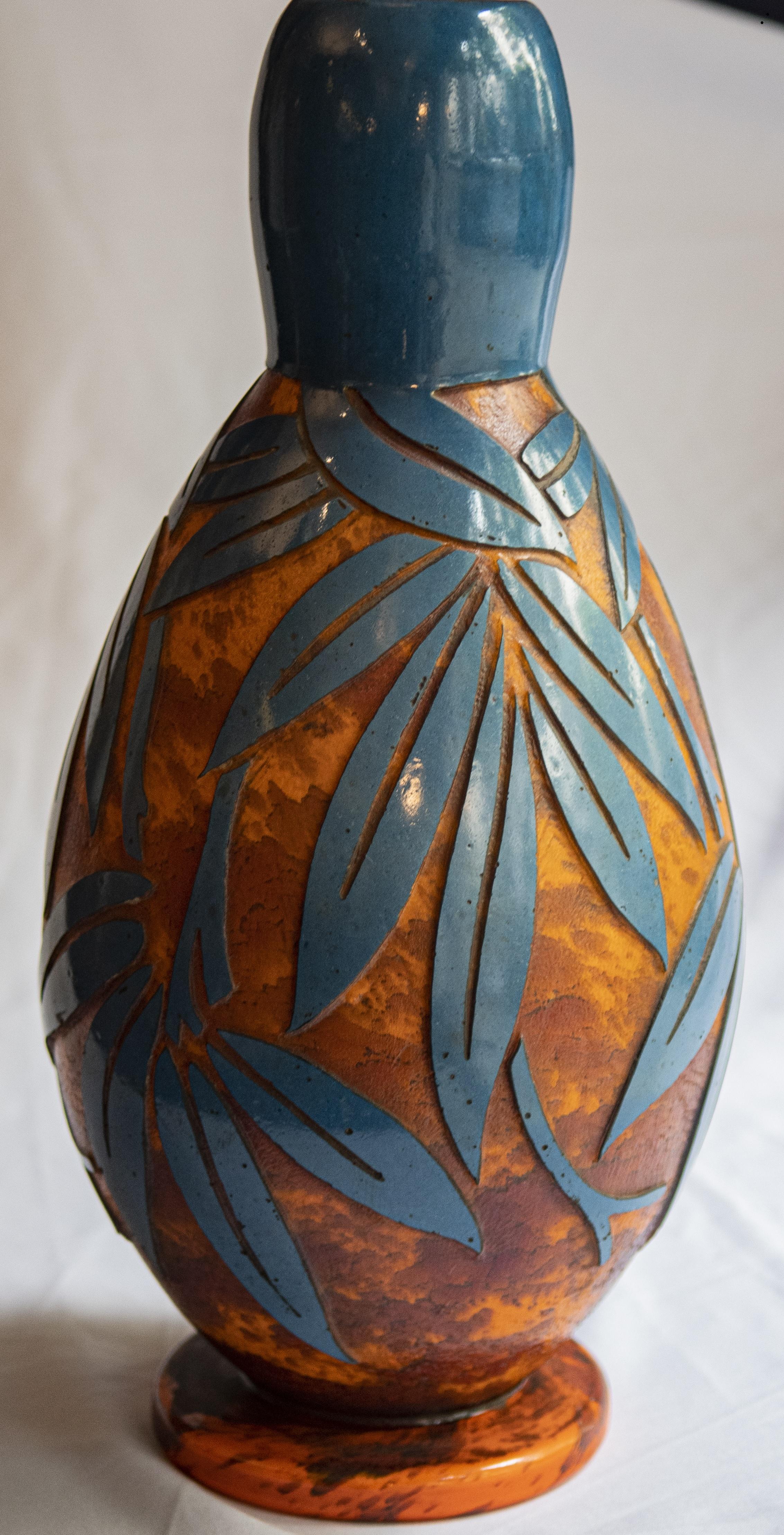 Entrez dans le glamour de l'ère Art déco avec cet exquis vase à fleurs français, orné de motifs complexes gravés à l'acide dans des teintes bleu clair et orange. Conçu pour évoquer l'opulence et la sophistication de l'époque, ce vase est un