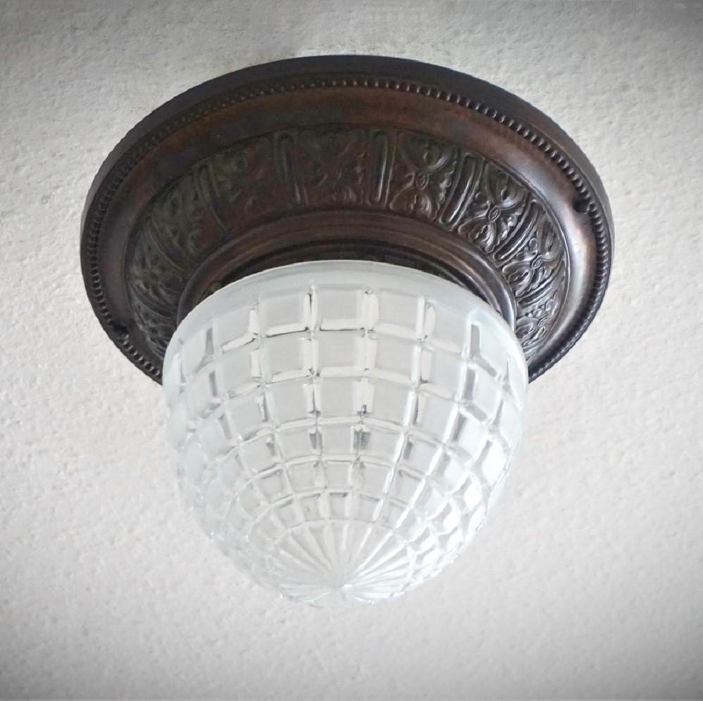 Art Deco ceiling light / flush mount with a patinated brass rim beautifully decorated with high relief rosettes fitted to a satin-cut glass lampshade, France 1930-1939. 
This ceiling light takes one E27 large sized bulb up to