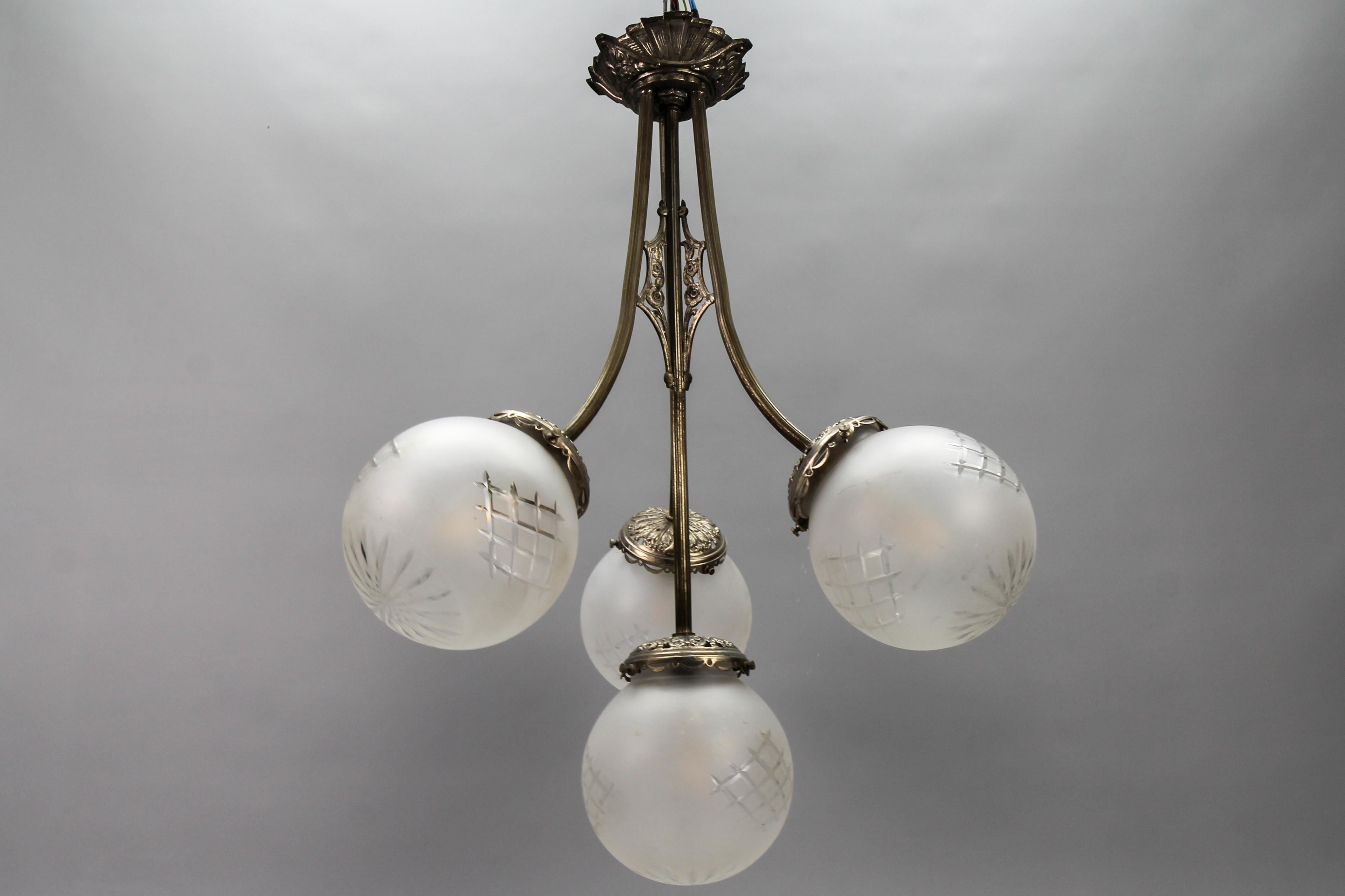 French Art Deco four-light brass and frosted cut glass globes pendant chandelier from circa the 1930s.
This elegant French Art Deco pendant chandelier features a brass light fixture ornate with Art Deco motifs and stylized flowers and four arms each