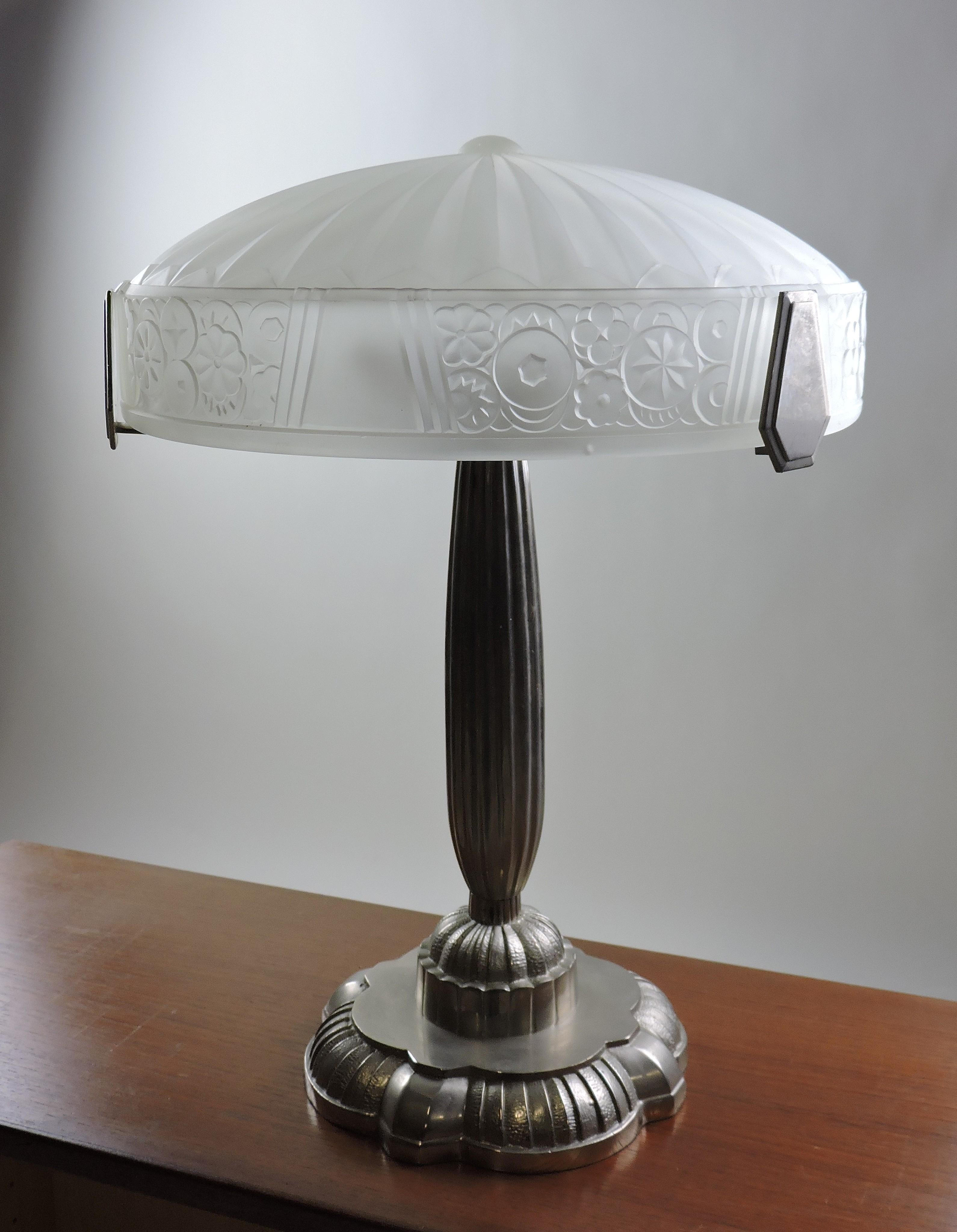 Beautiful French Art Deco table lamp with a etched glass shade that has a lovely stylized floral and geometric design resting on a nickel-plated base. A very high quality reproduction, it has European bulb sockets that have adapters so that it can
