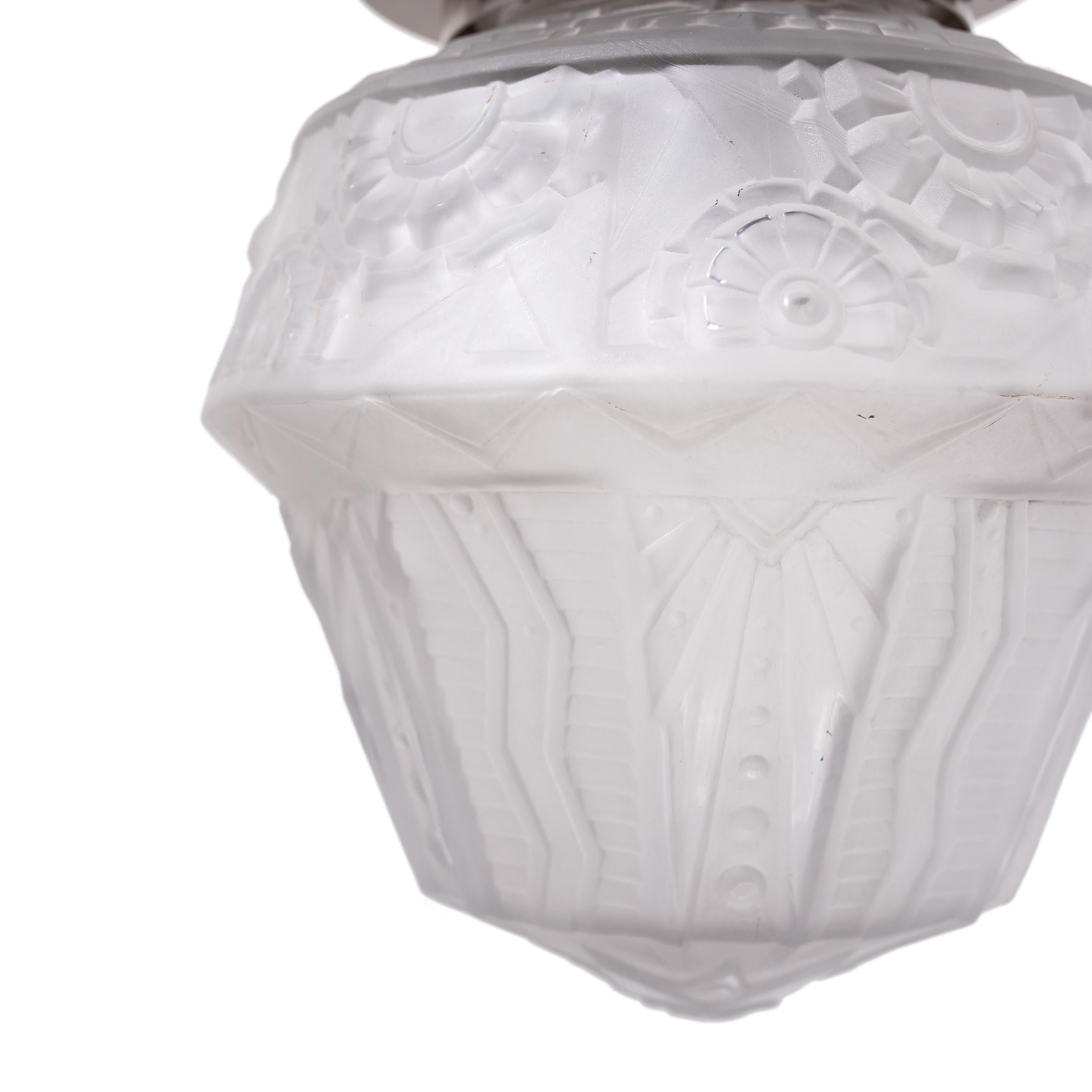 This early 20th century flush mount light fixture exemplifies French Art Deco lighting with its sculptural form and soft, delicate appearance. The ceiling light features a simple round flush mount and a frosted molded-glass shade shaped with