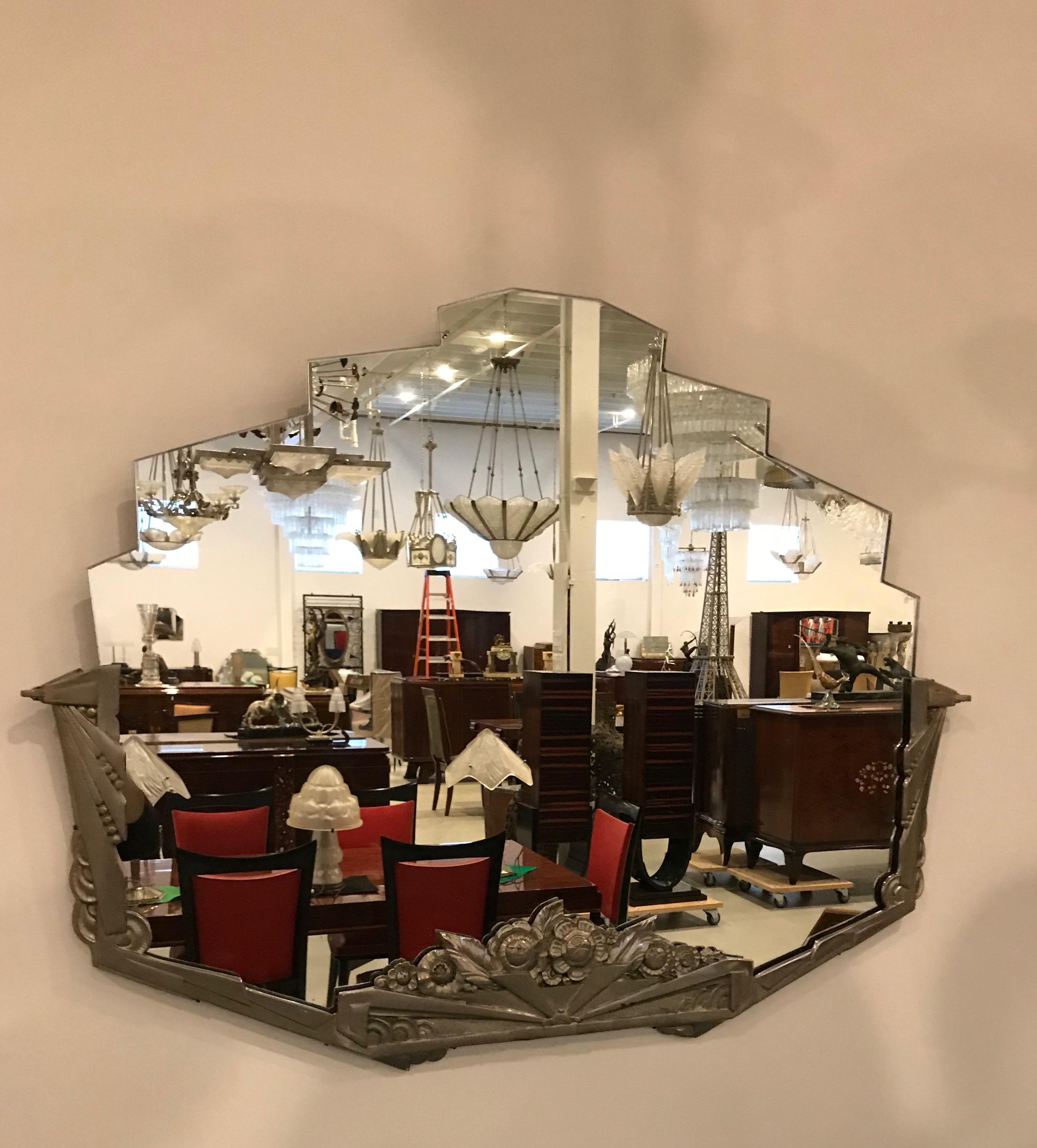 French Art Deco wall mirror with geometric and floral motif details. The frame has modest wear with signs of some patina. Re plating the frame upon request. The Mirror is in excellent condition.