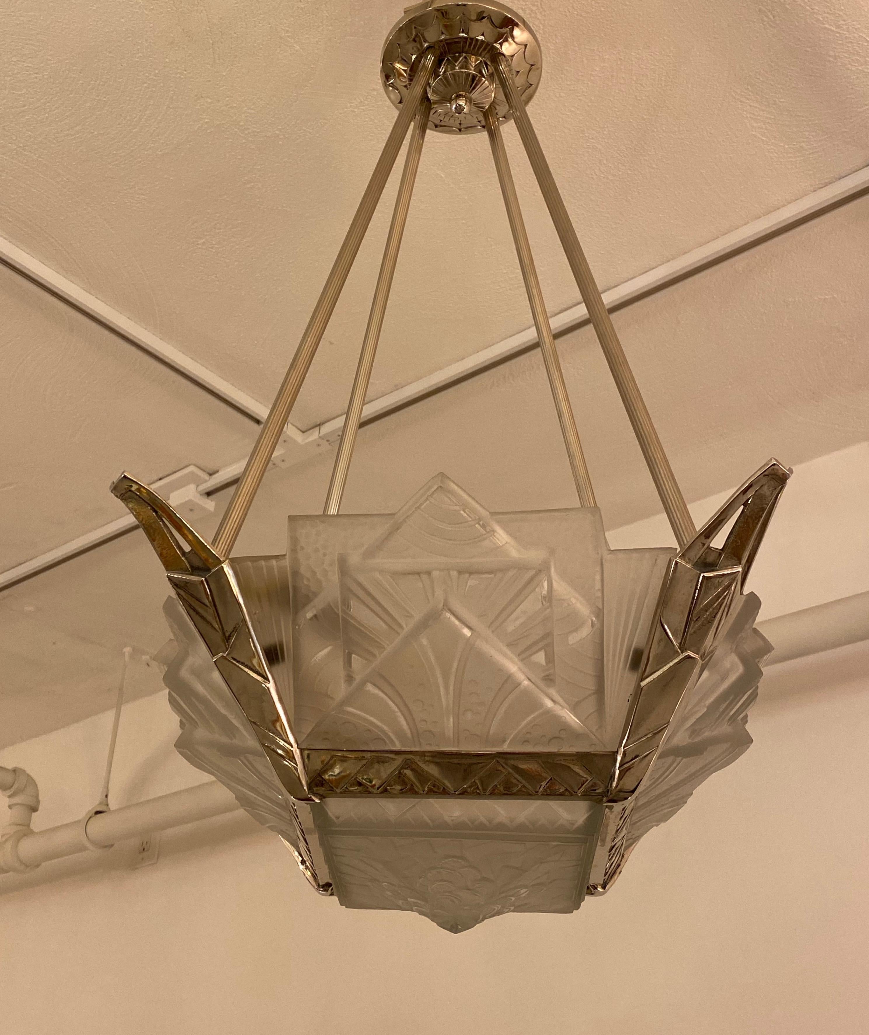 Stunning French Art Deco geometric chandelier signed by Muller Frères Luneville. Having clear frosted glass with over flowing geometric motif details. Supported by matching layered multi-tiered, geometric design polished nickel frame. Has been