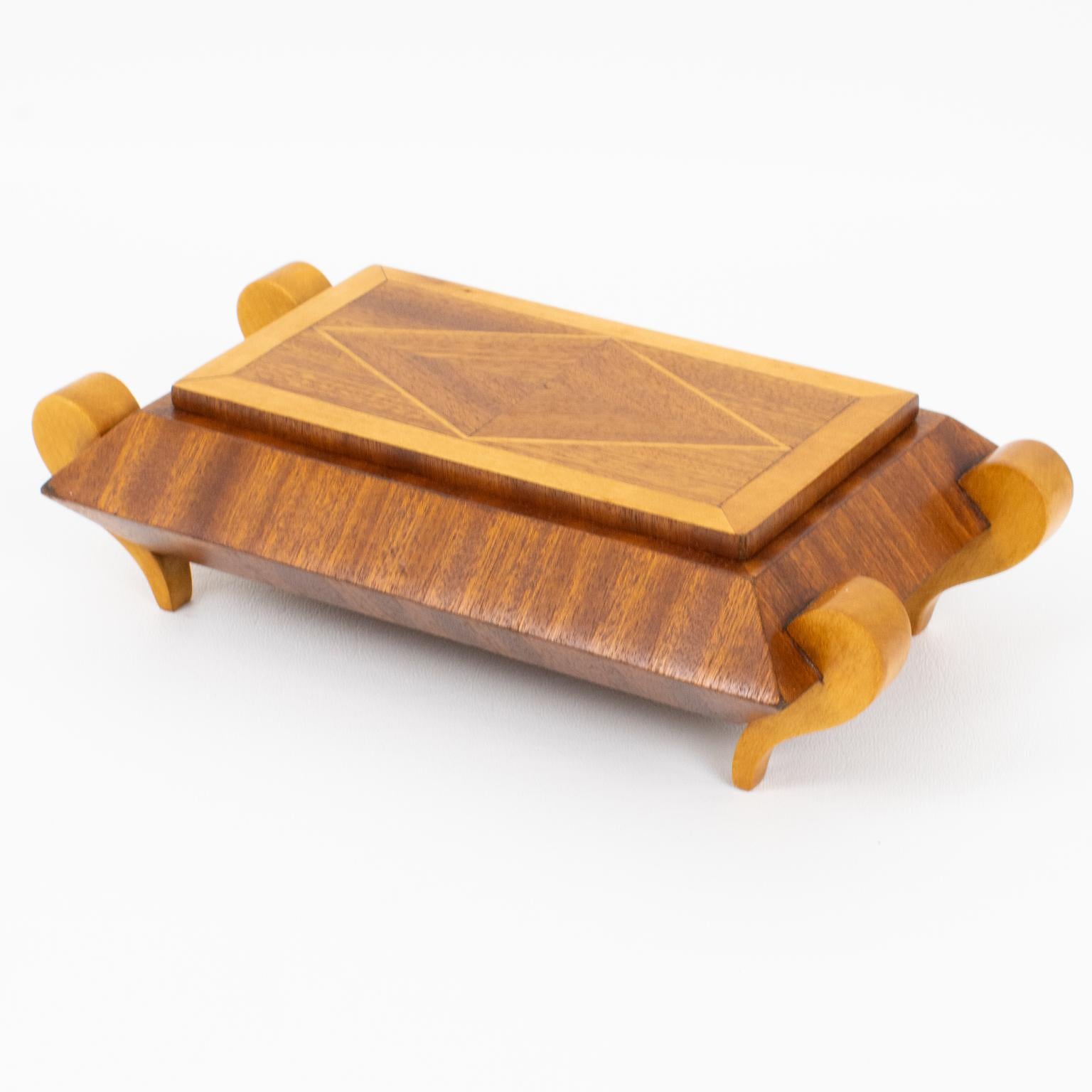 Esta impresionante caja ornamental con tapa y diseño de marquetería se fabricó en Francia hacia la década de 1930. Tiene un distintivo diseño en relieve con cuerpo rectangular y está compuesto de maderas tropicales lacadas, con marquetería