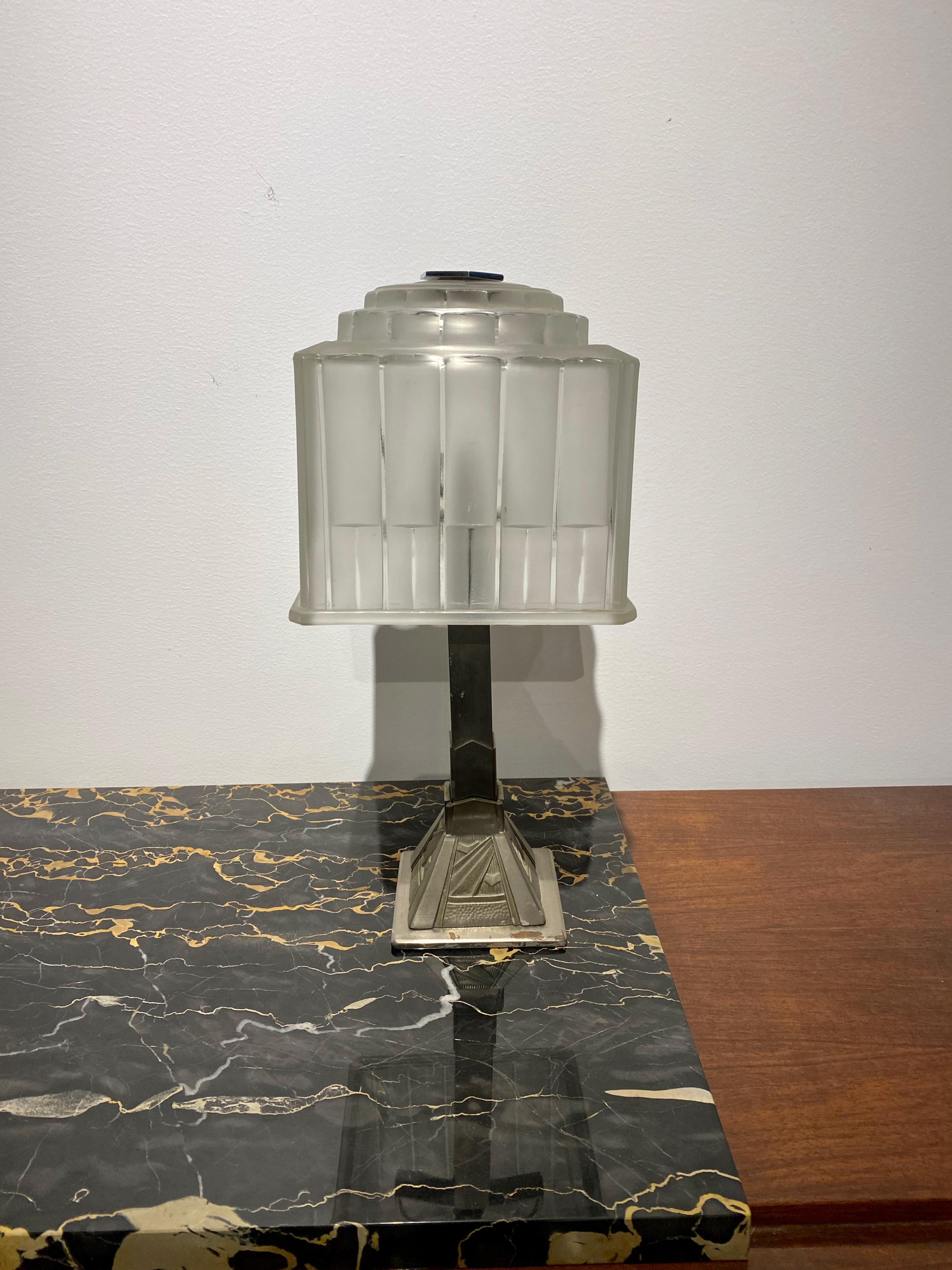 Single French Art Deco table lamp created by famous French artist Marius Ernest Sabino. The shade is clear frosted glass with polished details with geometric motif. Held by a nickel geometric base. Has been rewired for American use with one