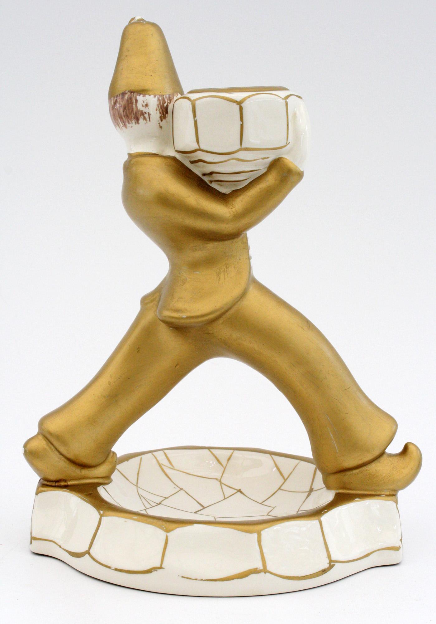 A charming French attributed Art Deco pottery figural candlestick portraying a novelty figure mounted on a circular base holding a large vessel on his shoulder which forms the candleholder. The figure is made in a cream colored pottery and decorated