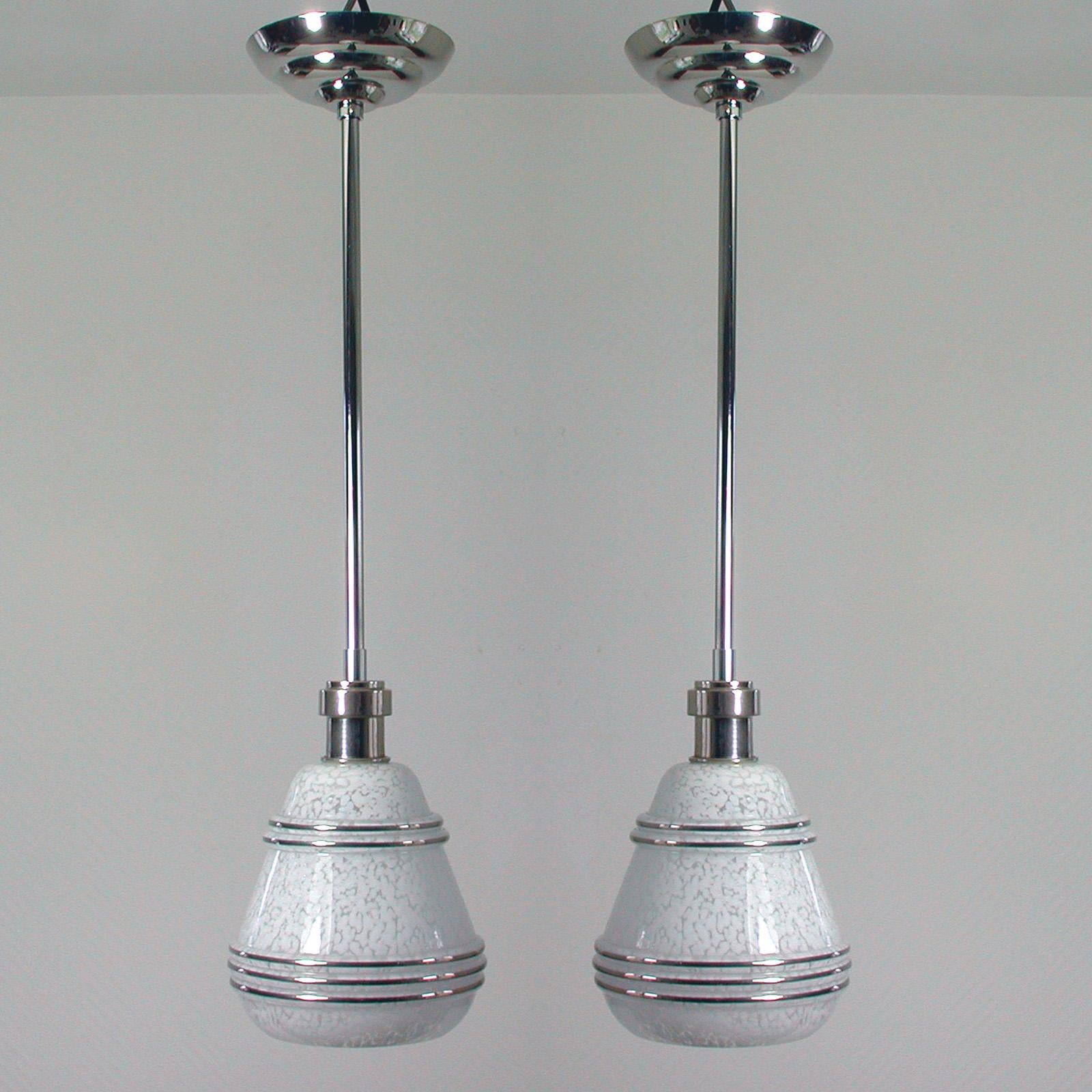This elegant set of 2 pendants was designed and made in France in the 1930s-1940s. The lamps are made of nickel plated metal / chrome and have got a mottled white glass shade with silver decor. 

The lamps can be used as pendants as well as flush