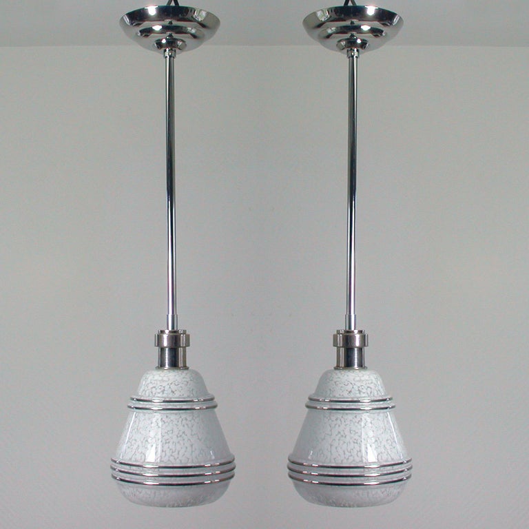 This elegant set of 2 pendants was designed and made in France in the 1930s-1940s. The lamps are made of nickel plated metal / chrome and have got a mottled white glass shade with silver decor. 

The lamps can be used as pendants as well as flush