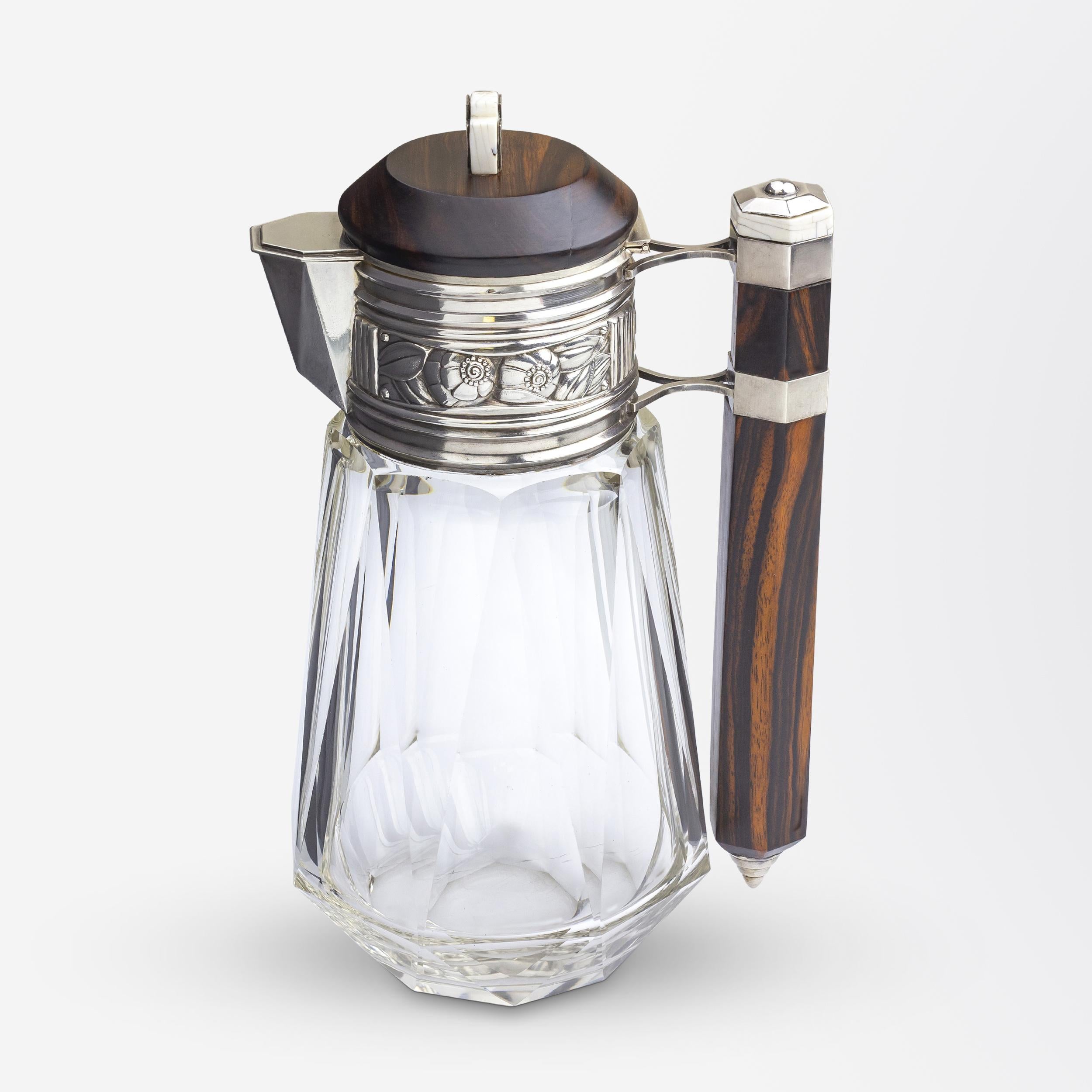 A French Art Deco ewer or pitcher crafted from thick-cut glass and macassar wood with a stylised silver floral frieze. The piece was crafted by Lagarde & Fortin of 5 Rue Froissart, Paris which was operating between 1922 and 1928. The piece is marked