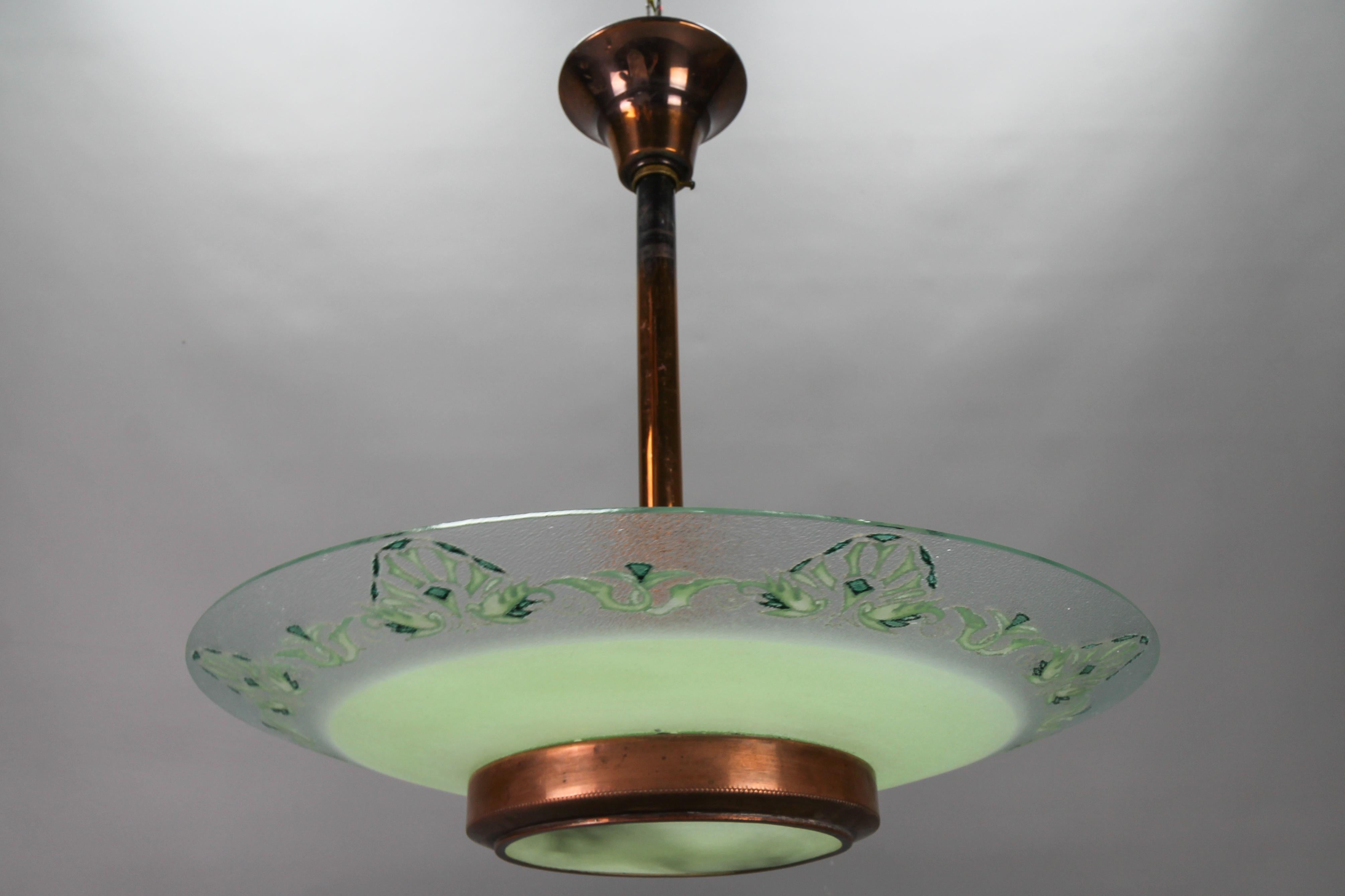 Französischer Art-Déco-Kronleuchter aus grünem Glas und Kupfer von Loys Lucha aus den 1930er Jahren.
Diese schöne Pendelleuchte hat einen leicht strukturierten Lampenschirm aus grünem und klarem Glas mit stilisierten Blumenmotiven auf dem klaren