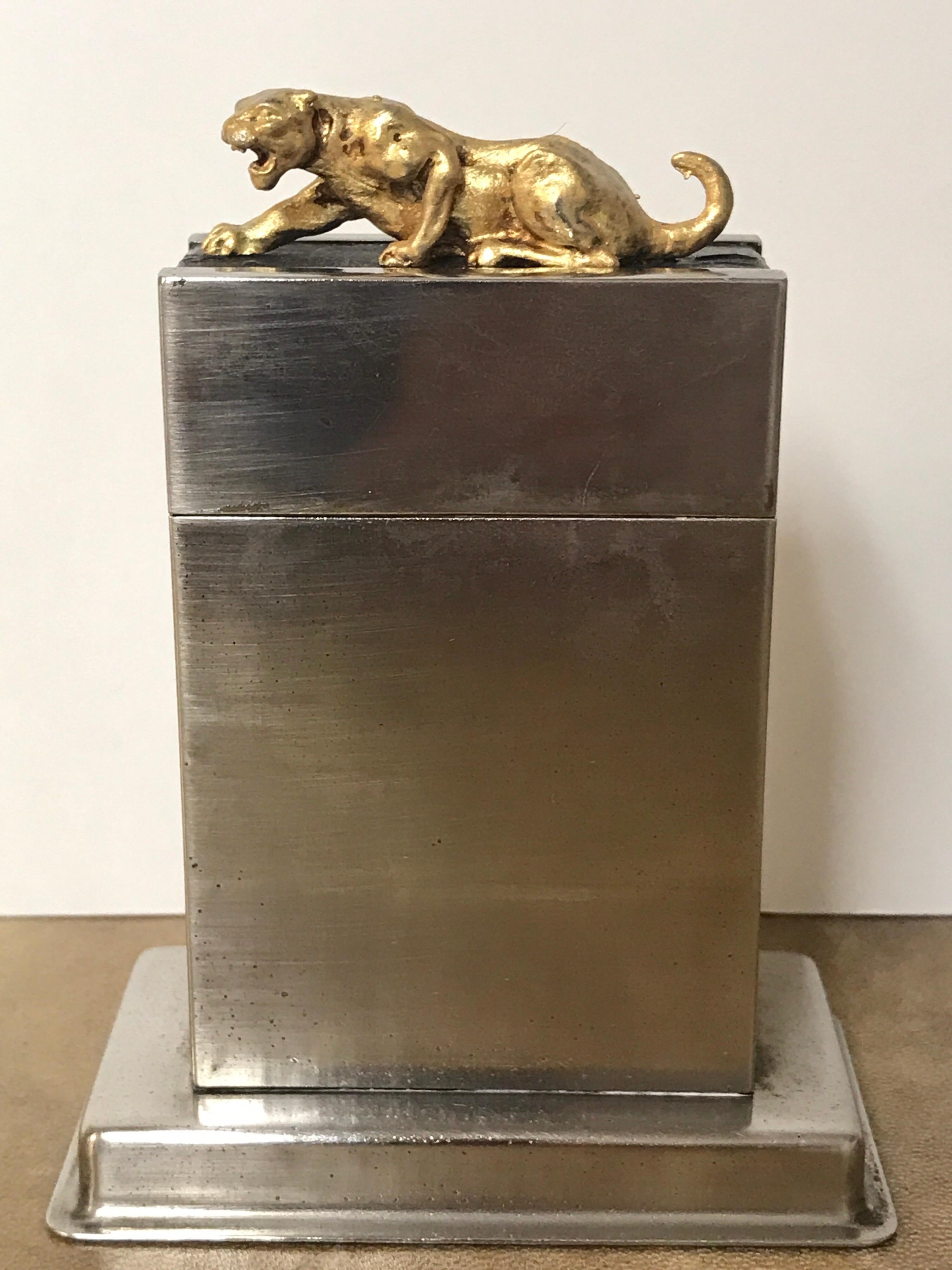 French Art Deco gunmetal and leather table box, of elongated rectangular form, the lid with a gilt crouching tiger resting on leather band. Wood lined, probably for cigarettes.