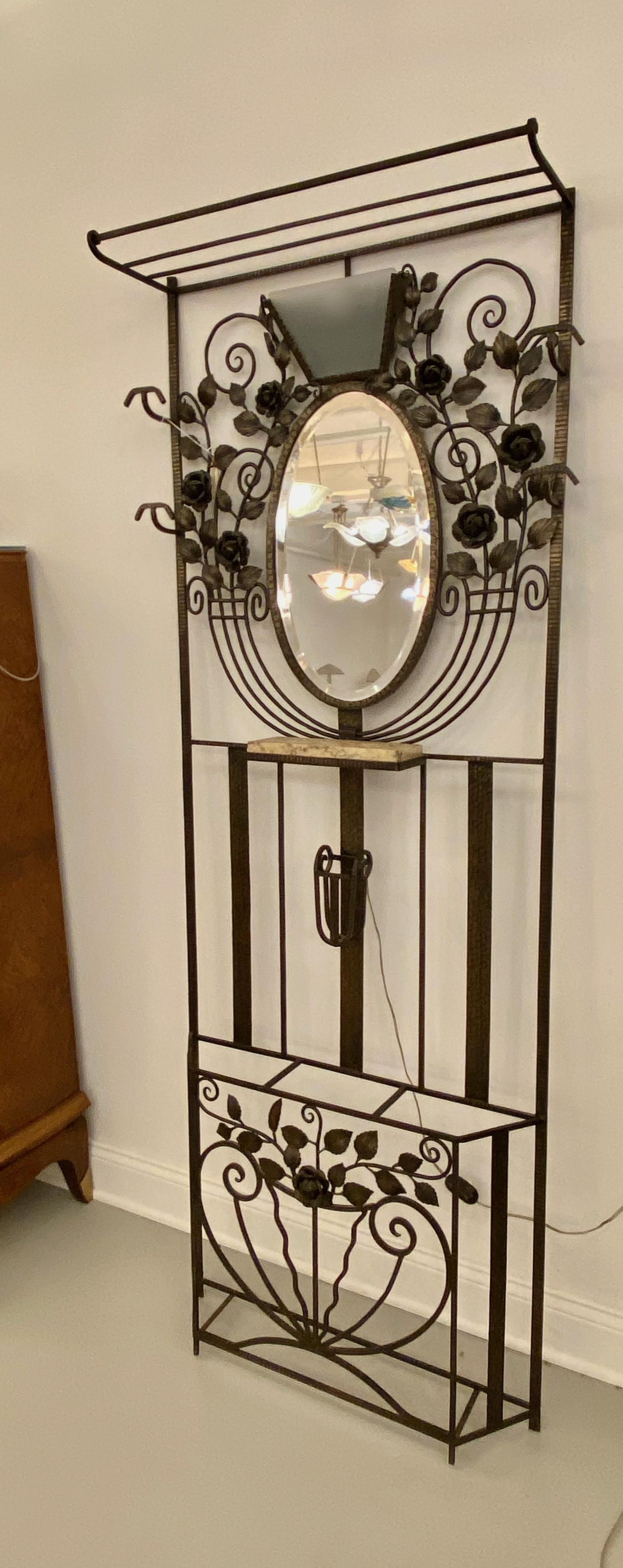 French Art Deco hall tree with glass sconce. Having four coat hangers with umbrella stands, center oval mirror and hat rack. Above the center mirror there is a frosted glass light. Below the mirror there is a marble shelf. The frame having Deco