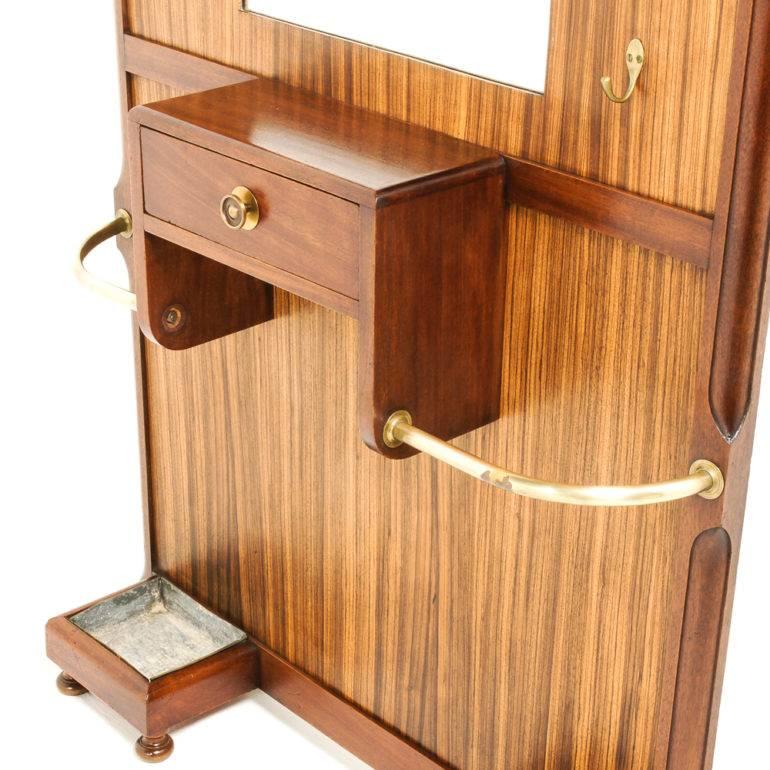 An unusual French Art Deco hallstand with a dramatic curved profile, framed in solid mahogany and veneered in zebrawood, having hooks for coats, a mirror over a small drawer, and with two lower side-sections for umbrellas and walking sticks, circa