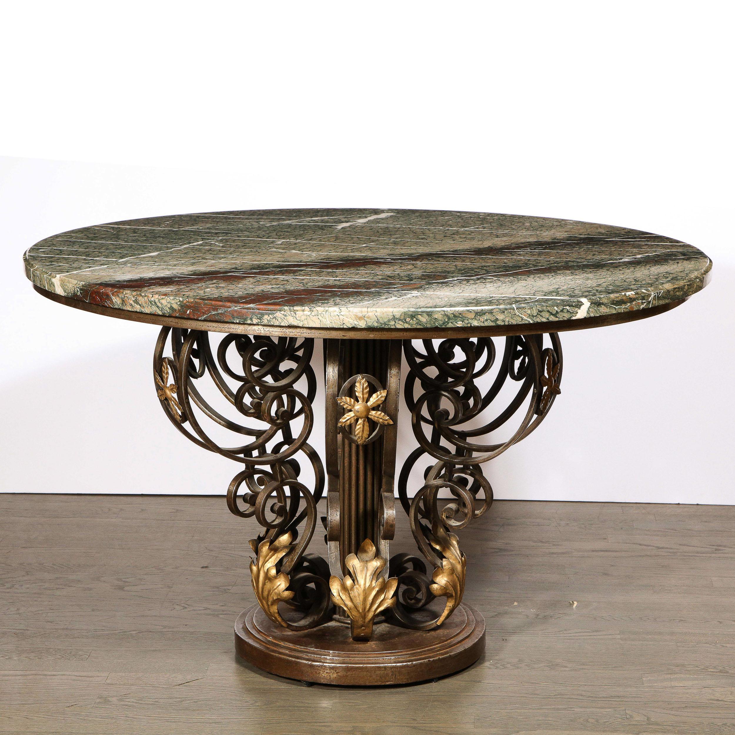 Created in the manner of Gilbert Poillerat, this stunning Art Deco table was realized in France circa 1940. It features an intricate sculptural base in hand wrought iron with stylized foliate gilded accents throughout. The beveled circular top is