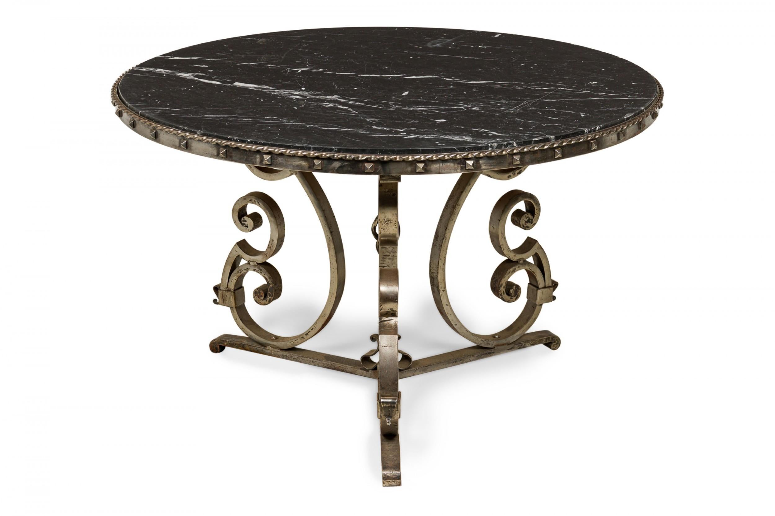 French Art Deco center table with a scroll form iron pedestal base with rope design trim and base finial and square iron studs around the tabletop frame, supporting a thick circular black marble top. (manner of RAYMOND SUBES).