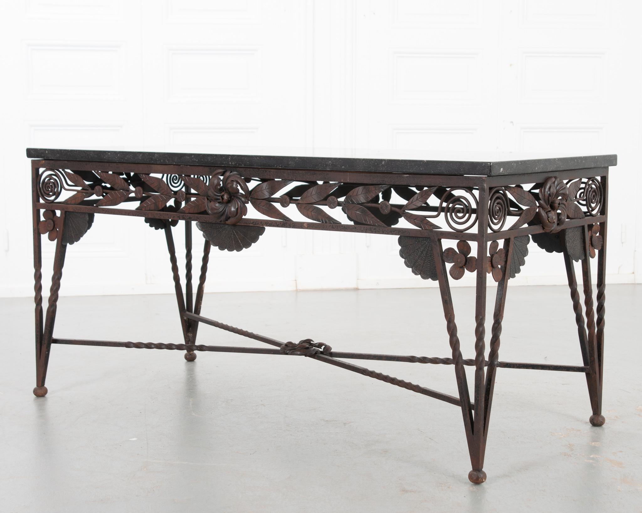 A stunning Art Deco cocktail table from 20th Century France. The black, fossil marble top is removable and sits perfectly on its symmetrical iron base. Each side features large center flowers, flanked by detailed leaves that swirl tightly into each