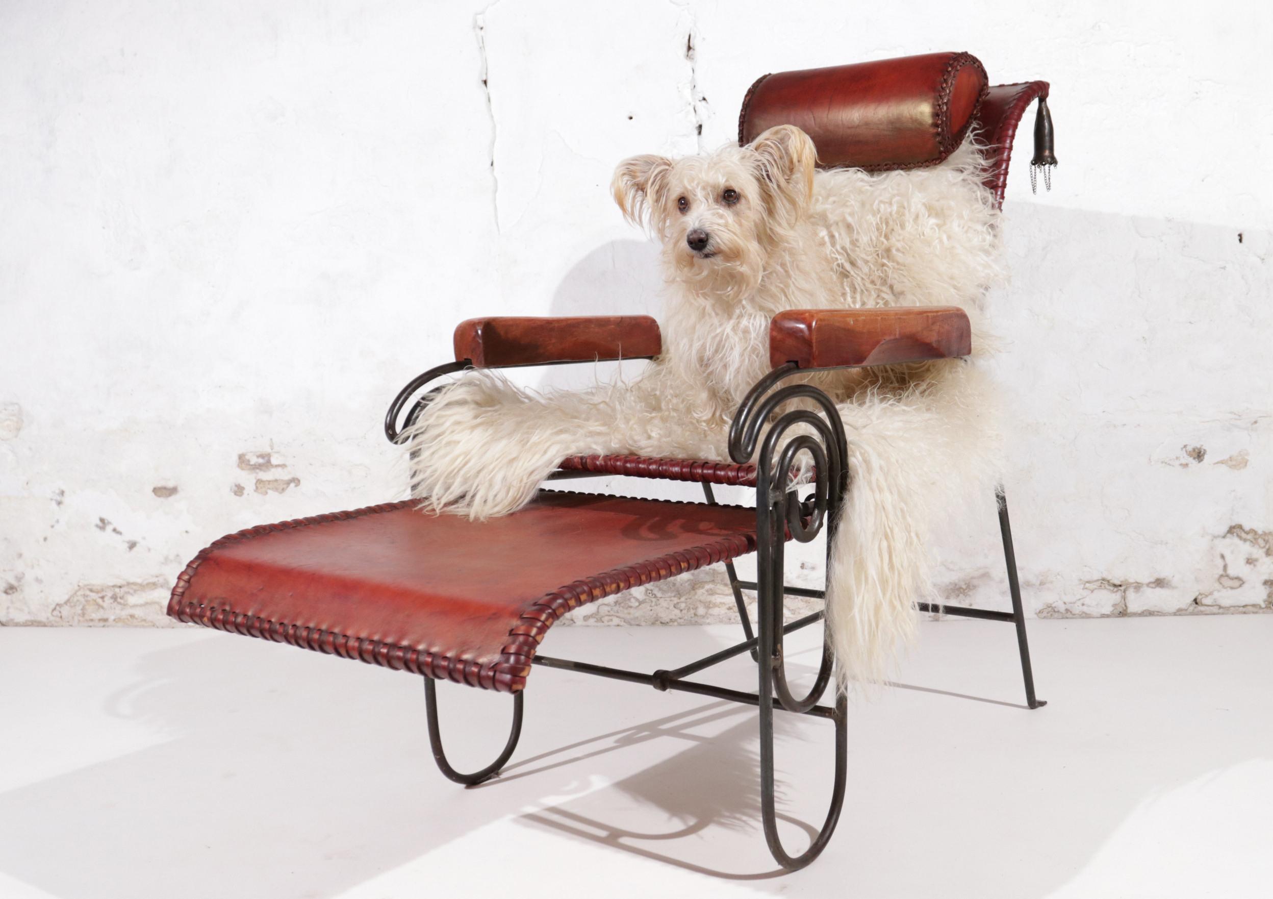 Avant-garde leather and iron lounge chair with leather tied upholstery, wrought iron frame with pull-out foot rest; wood carved arm rests and bronze tassels at the top back.

  