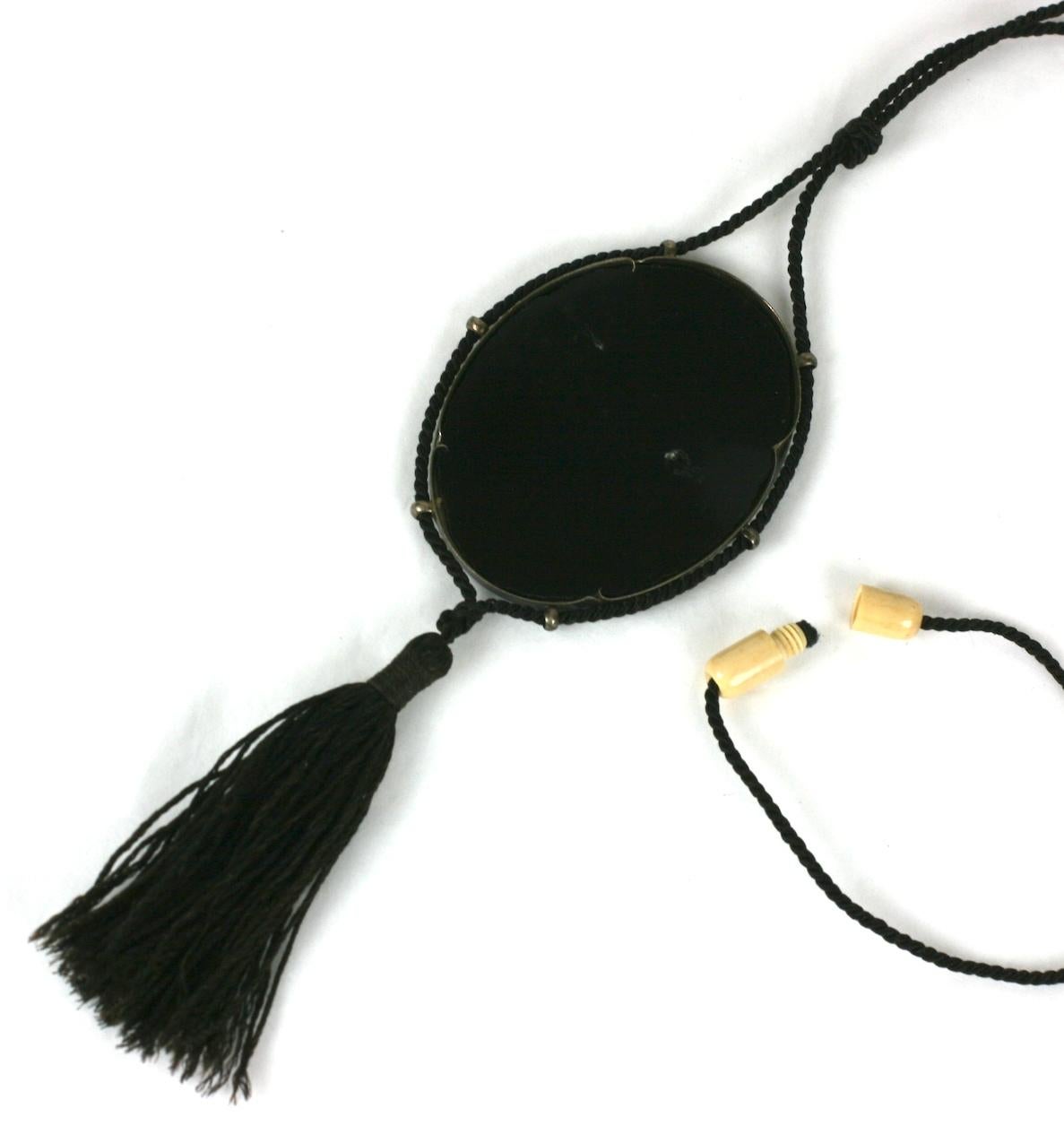 French Art Deco Japonesque Pendant Necklace of finely carved faux ivory colored celluloid backed by an oval panel of black bakelite. Set in a silvered metal frame with six round loops, suspended with a silk cord with decorative tassel.
Barrel clasp