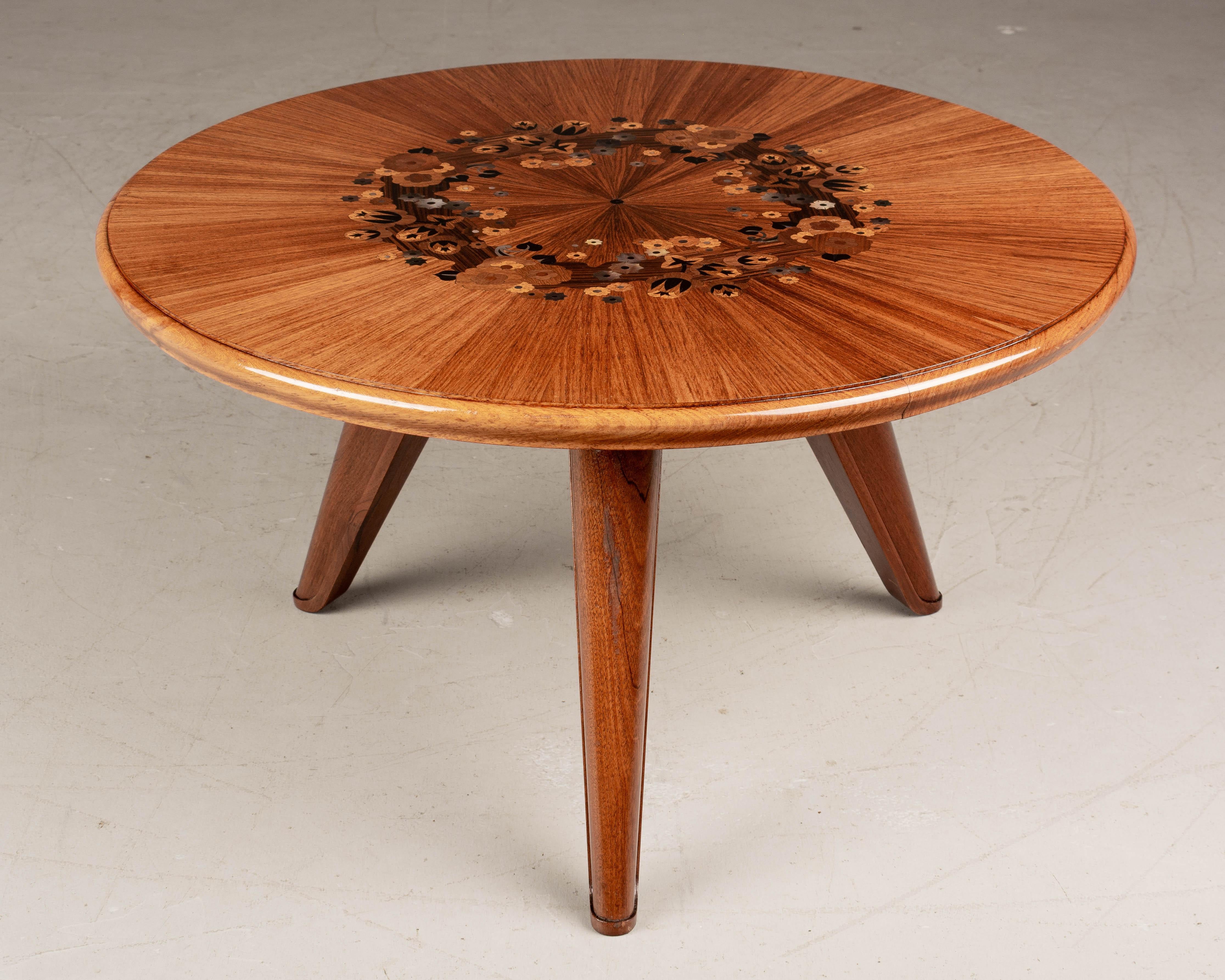 A small French Art Deco Jules Leleu attributed coffee or cocktail table. Stylized floral marquetry top with inlaid maccassar, rosewood, mother of pearl and satinwood. Resting on a sturdy mahogany tripod base. Exceptional quality and craftsmanship.