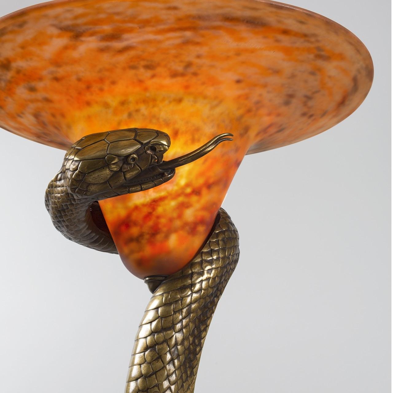 A French Art Deco serpent lamp by Edgar Brandt and Daum titled “La Tentation”. The lamp features a bronze cobra with a rich golden brown color. The snake is almost completely vertically extended, standing on the lid of a woven basket. Its head