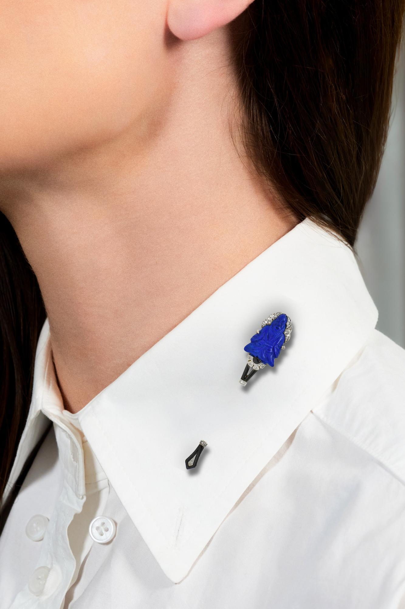 Designed as a jabot style bar brooch featuring a carved lapis terminal
Depicting a stylized Buddha figure measuring 13.0 x 20.0 mm
Opaque ultramarine blue in color with gold pyrite flecking
Accented by geometric segments glossed with black enamel -