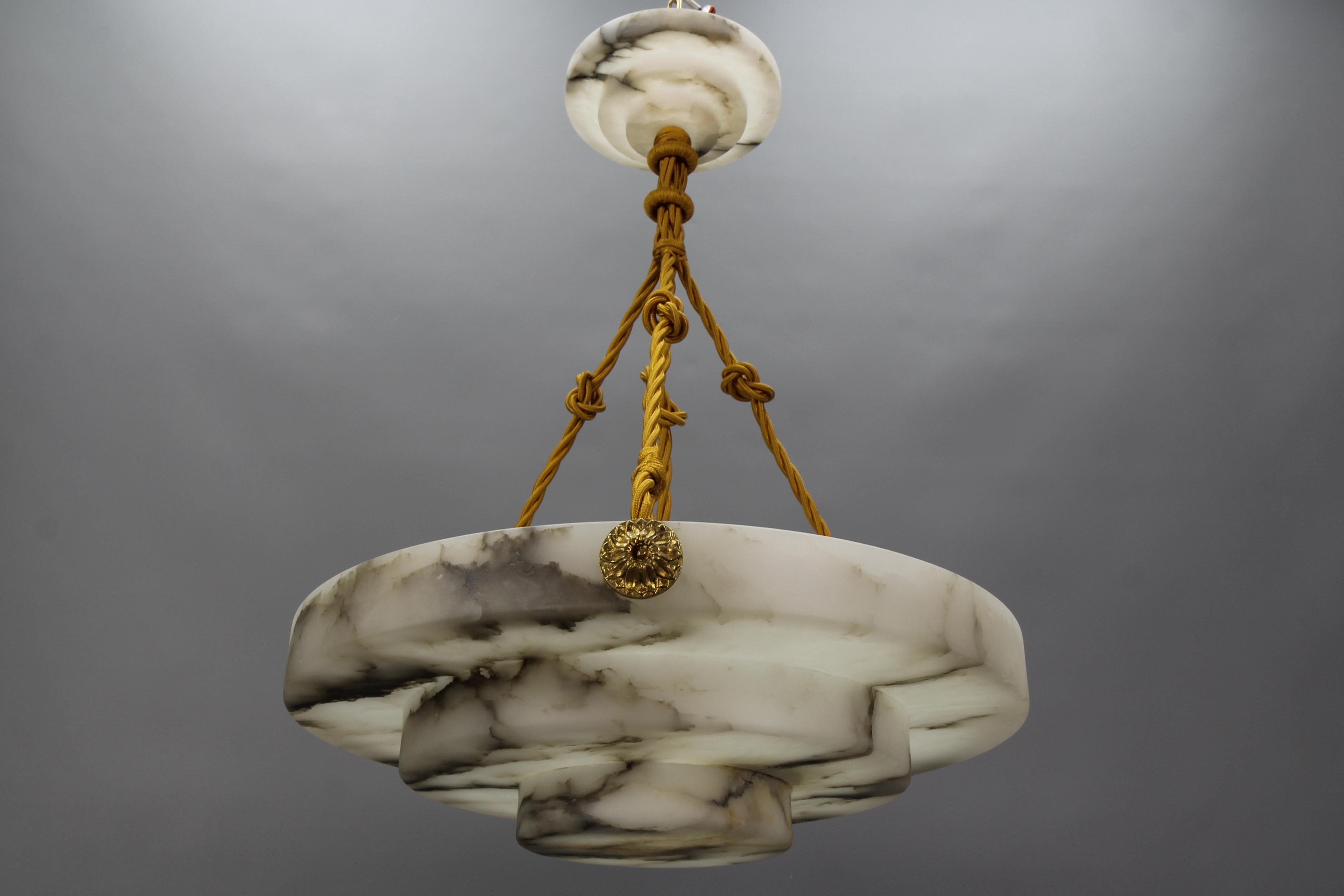 An elegant, round, layered Art Deco ceiling pendant light featuring a lampshade - a bowl - of white alabaster with dark brown and black veins. France, around 1920.
Masterfully carved in layered form, this beautifully veined one-piece alabaster bowl