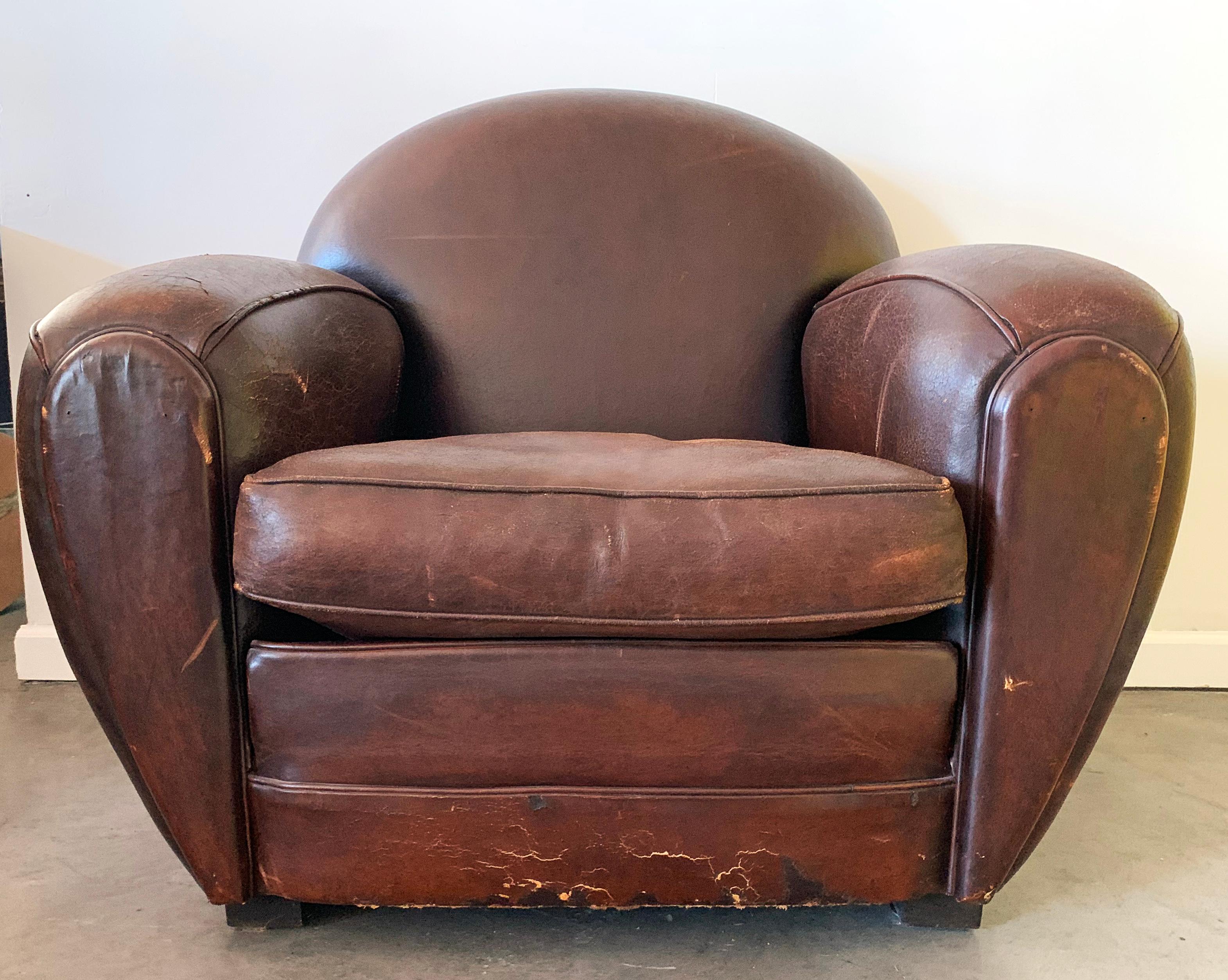 An absolutely round Art Deco leather club chair. This leather club chairs were purchased in the 1980s in Paris at the Les Puces de Saint-Ouen. The chair was re-dyed about 4 years ago and is in stunningly distressed condition with a wonderful patina