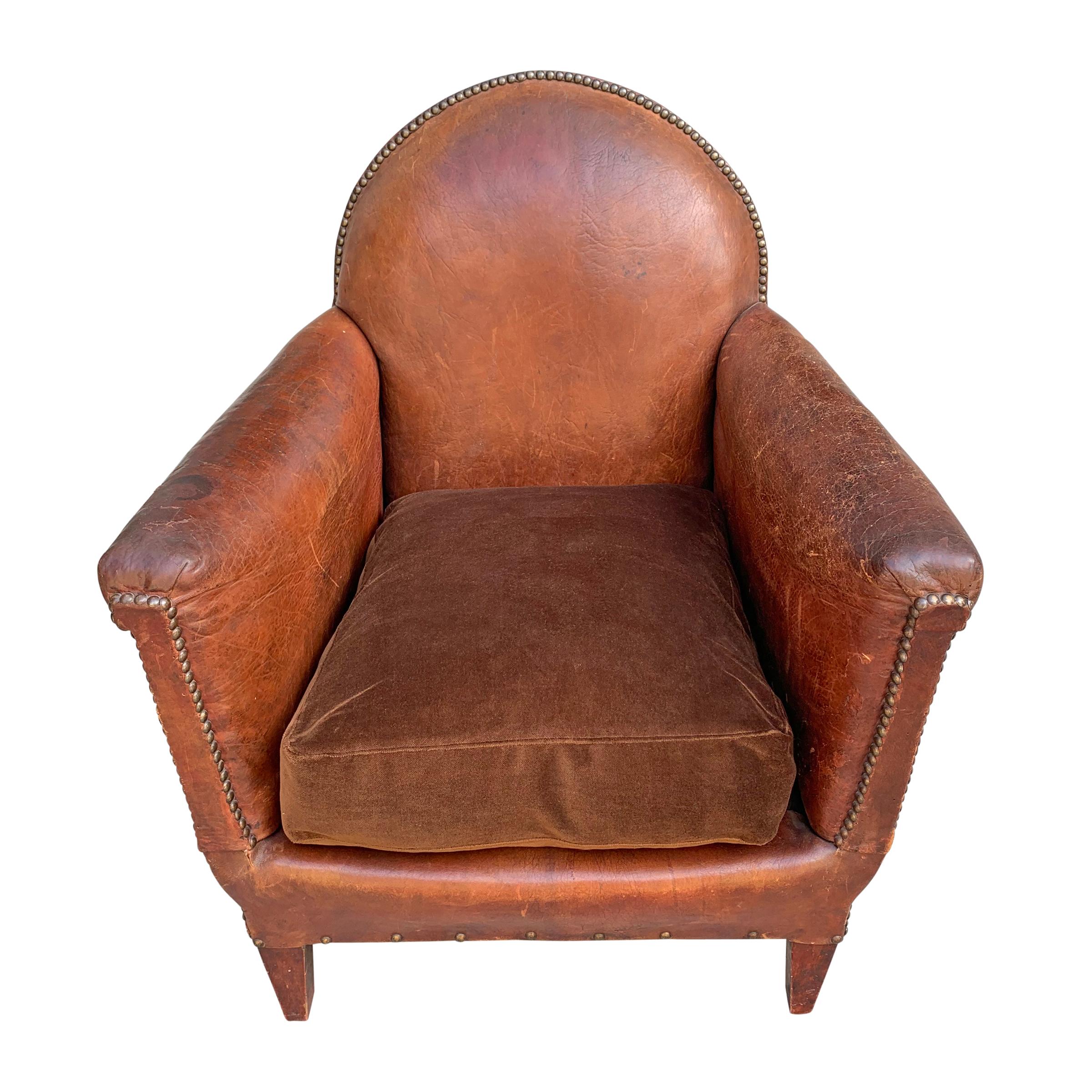 A handsome early 20th century French leather club chair with a tall round back, nailhead trim, and a down filled brown velvet seat.