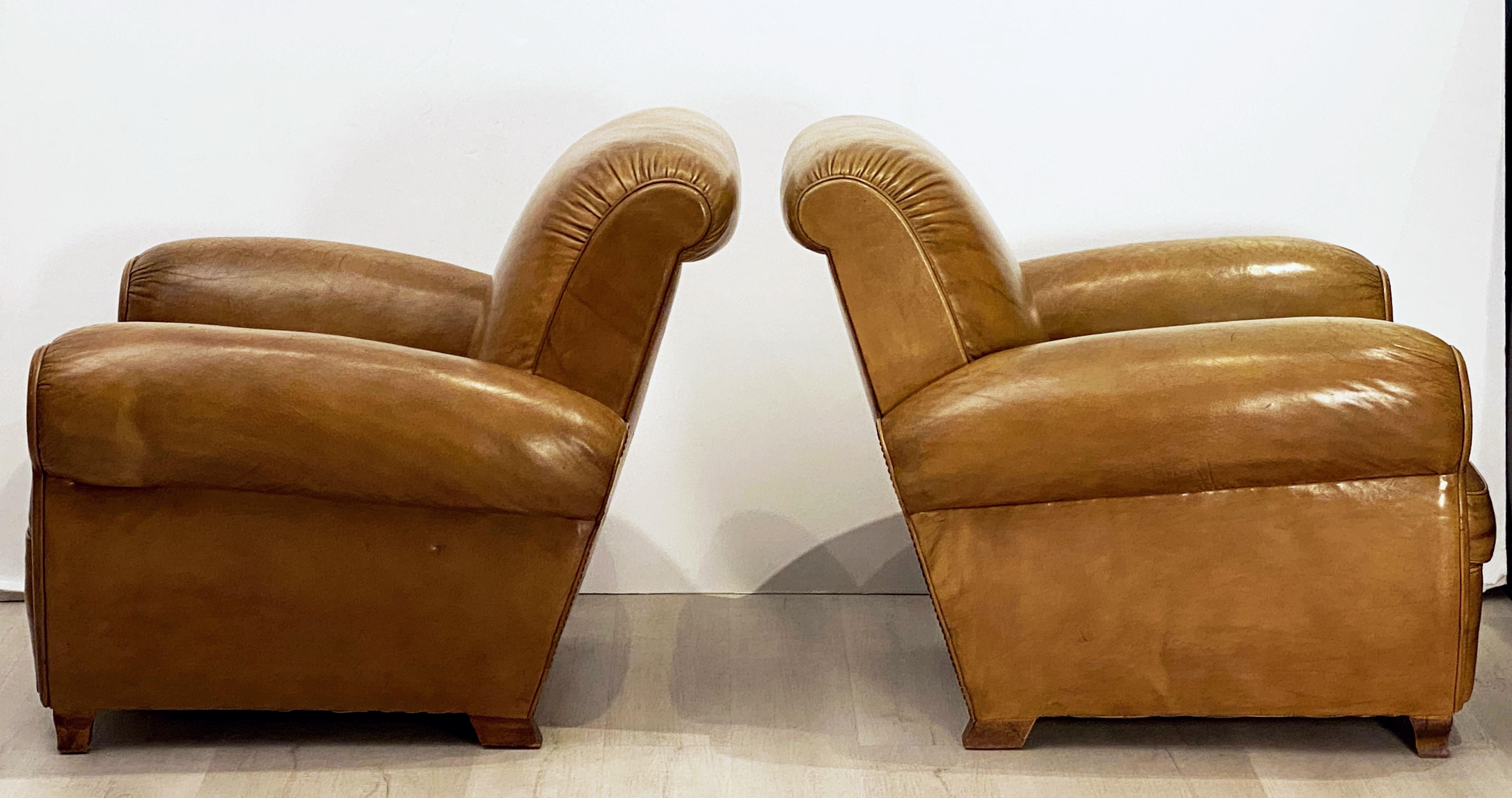 A handsome pair of vintage French leather upholstered club or lounge chairs from the Art Deco era - each chair featuring a comfortable back and seat with removable cushion, with stylish arms and original leather, brass nail-head trim to back, and
