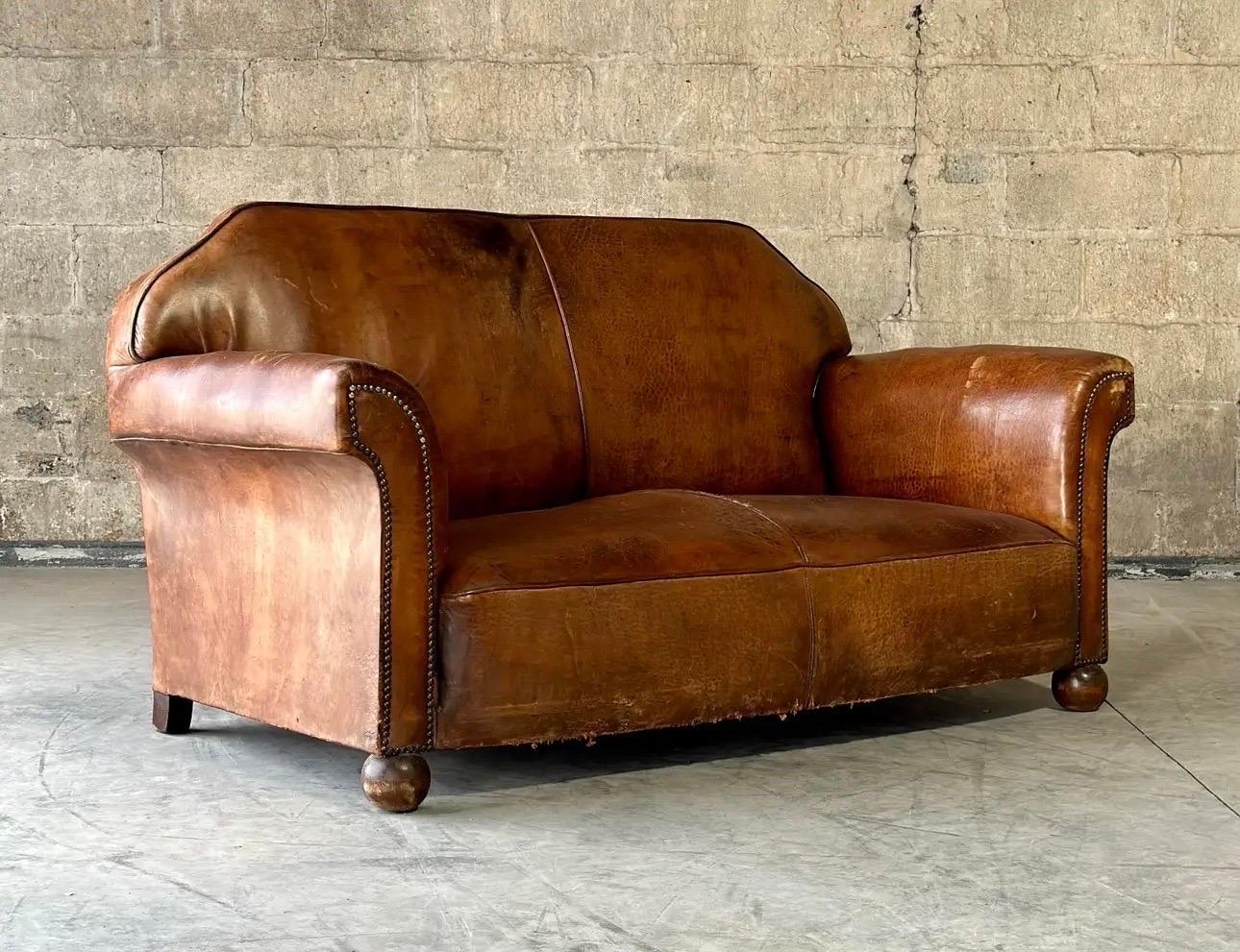 An Art Deco period sofa from France. Gorgeous wear on the original leather, with spectacular angles throughout, studded with a nailhead trim. Has the original ball feet in front.