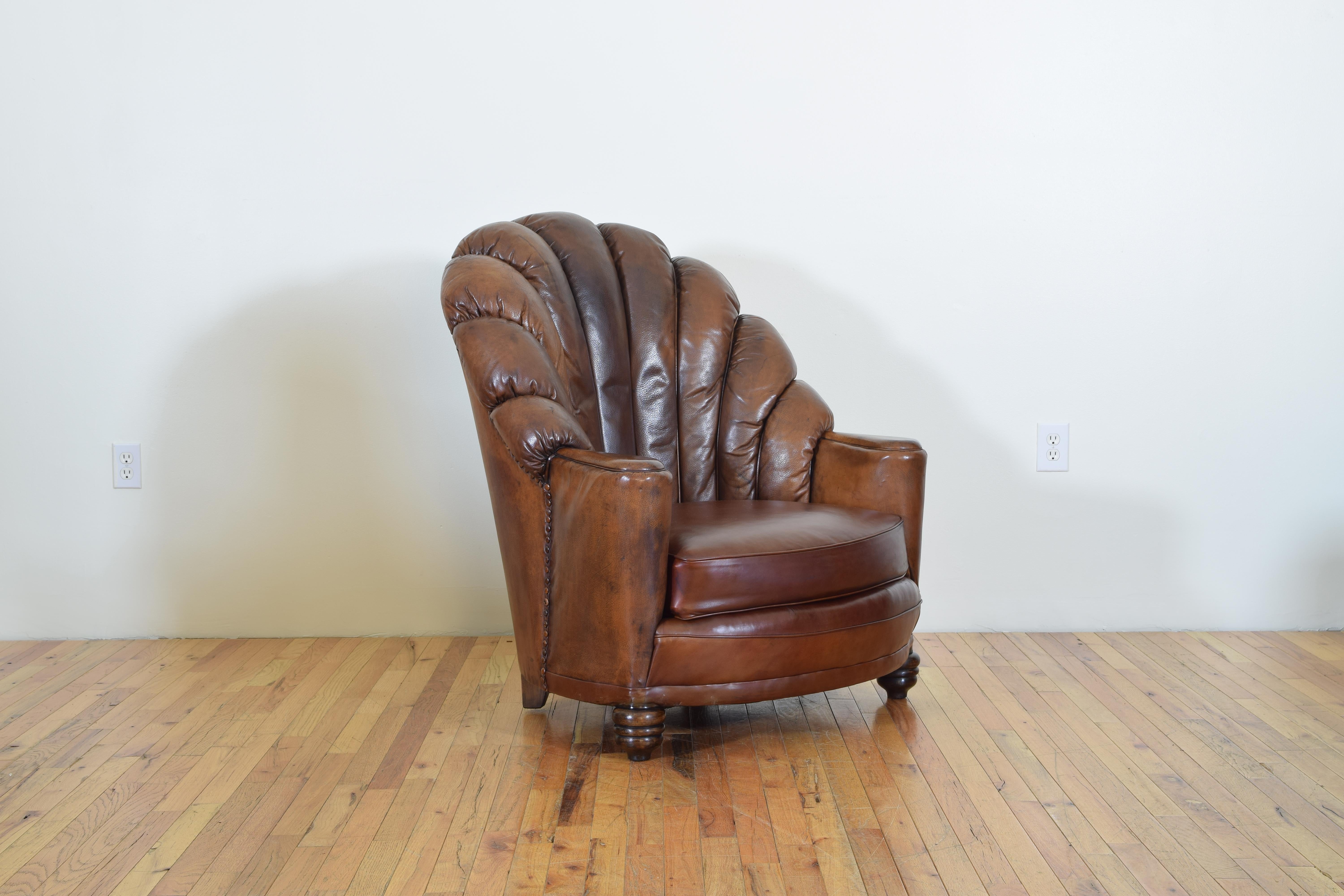 Having a fanback wing and a loose cushion, trimmed in leather covered nailheads, raised on turned wooden feet.