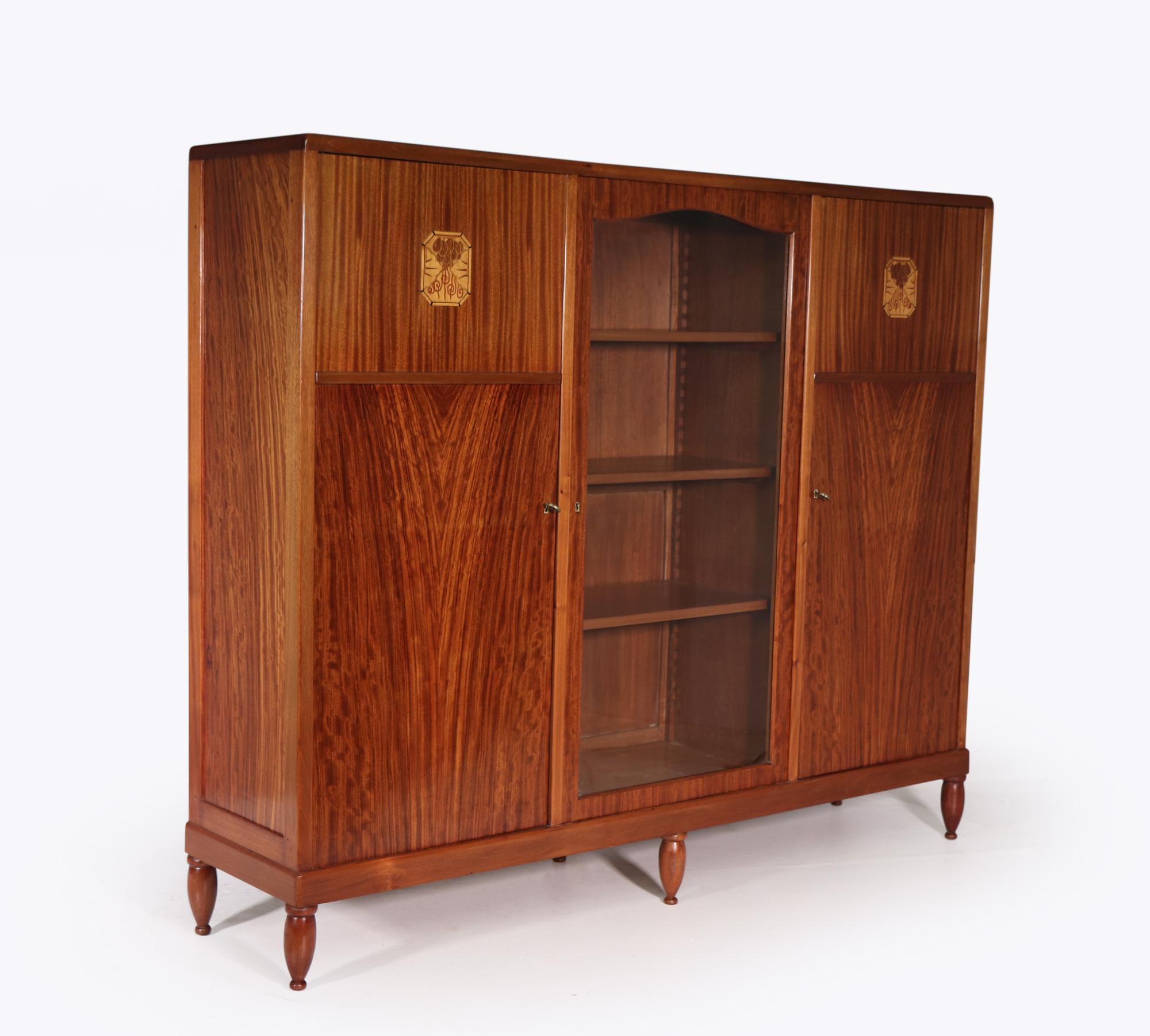 A French Art Deco Library bookcase in Mahogany and other exotic veneers, the emblem on the two blind doors is excellent work the cabinet has nine adjustable shelves so plenty of room to fit your favorite books, the glazed central section still has