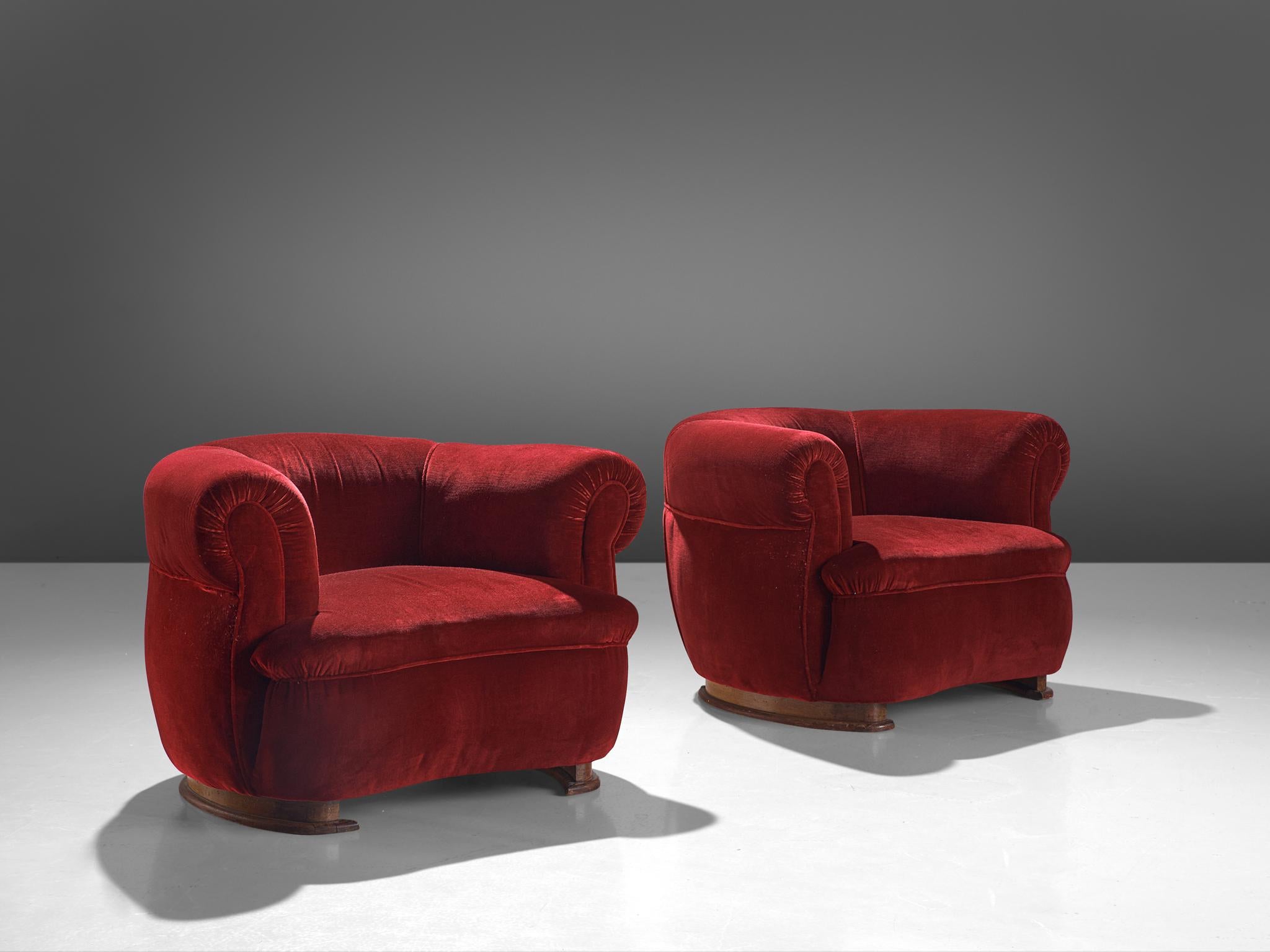 Pair of French lounge chairs, red velvet upholstery, oak, France, 1940s
 
These exquisite pair of lounge chairs of French origin undoubtedly breathes the late Art Deco Period of the 1940s. The design has a certain theatrical aesthetic with curved