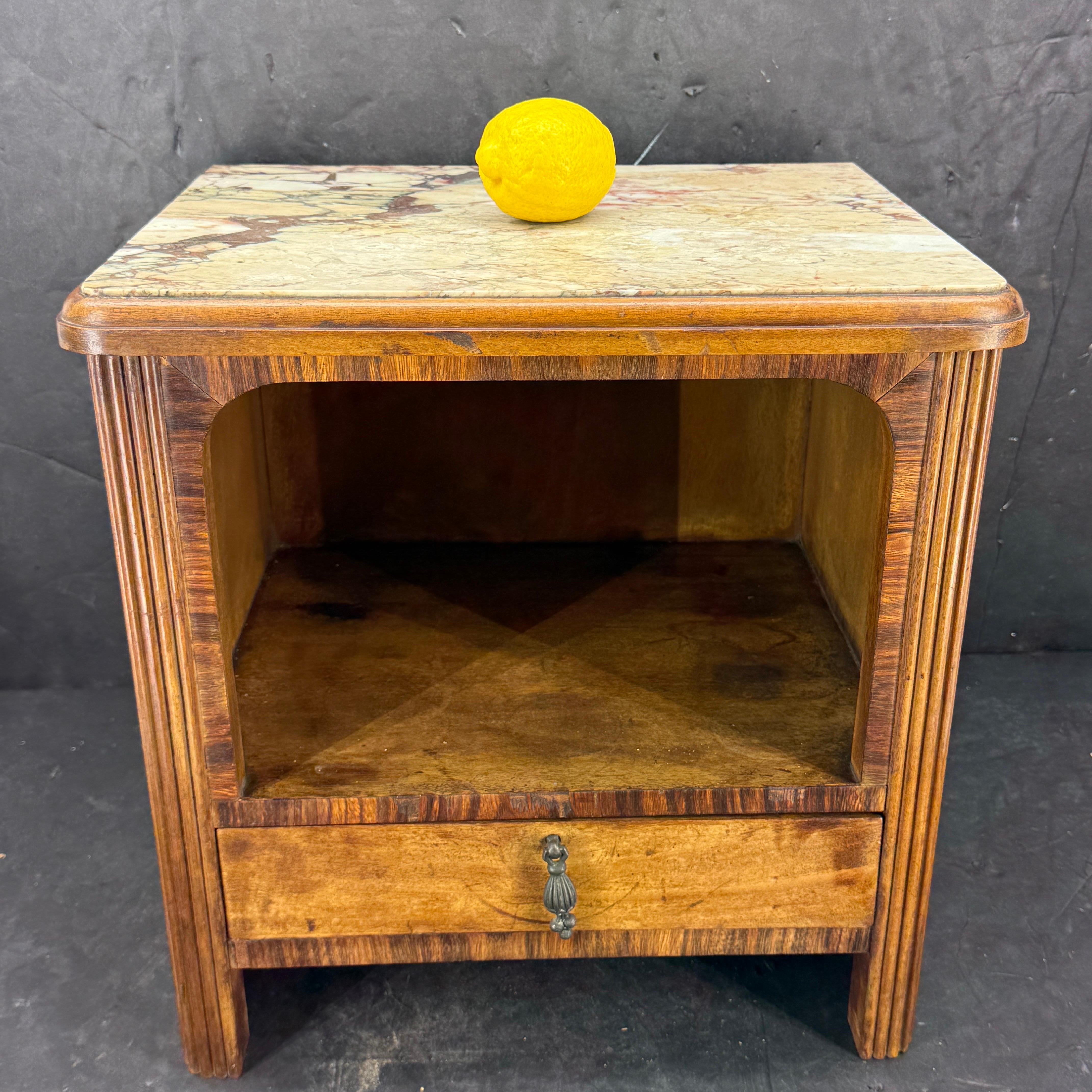 Very charming low wooden Art Deco nightstand side table featuring an open cabinet space and one drawer with original hardware. Additionally the nightstand features a marble top and fluted sides. We see this table being featured in a modern or formal