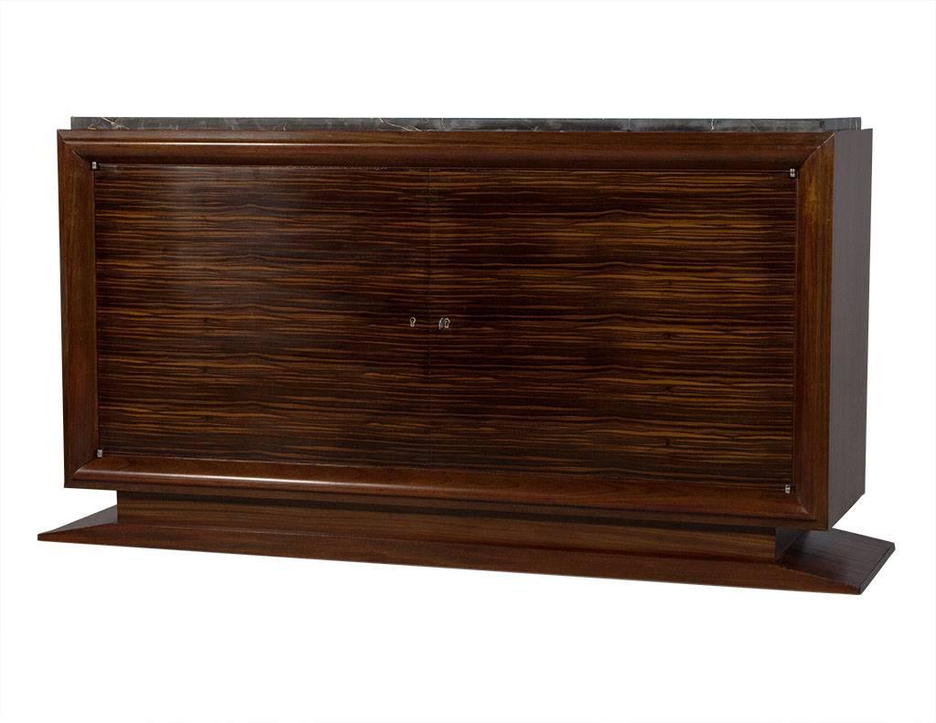 This Art Deco style sideboard is a truly luxurious piece. It sits atop a sloped, plinth base with the original black marble top and creamy brown veining throughout. It has been retrofitted with shelving and storage for a media unit, and has a deep
