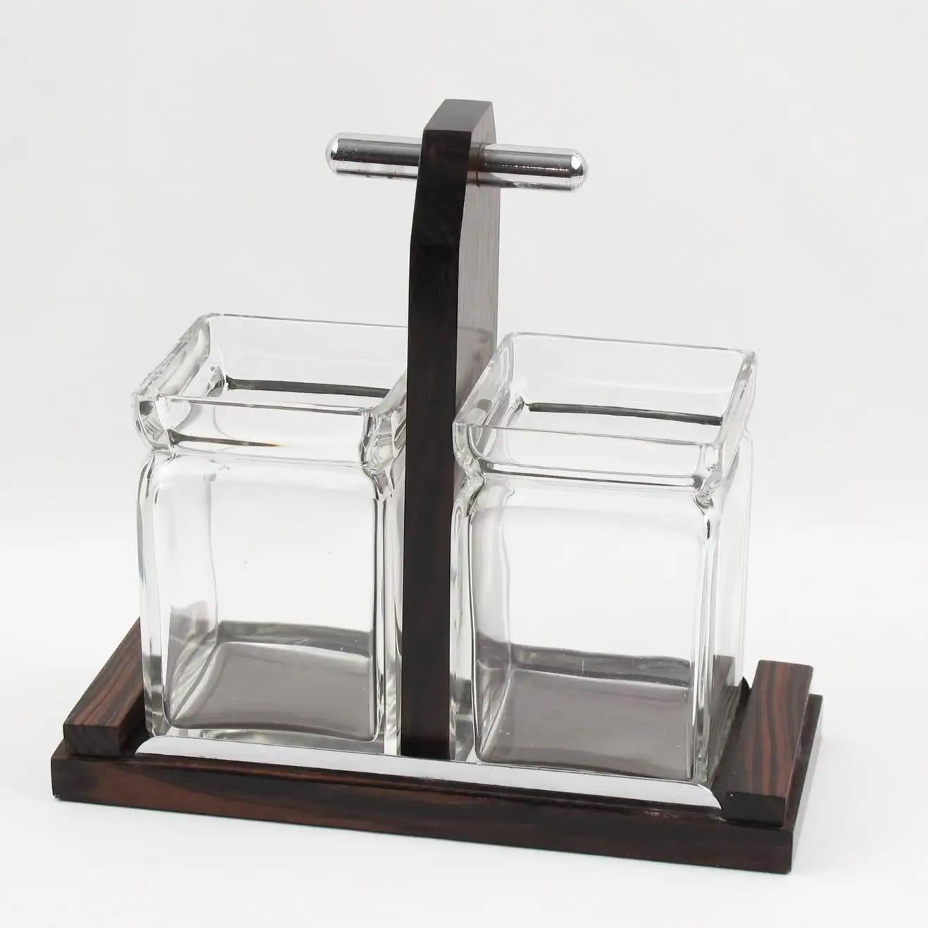 This is a lovely Art Deco tableware preserves, pickles, or condiments set on a stand with crystal jars. The serving set features a modernist design with a Macassar wood and chrome geometric base complimented with a tall handle. There are two