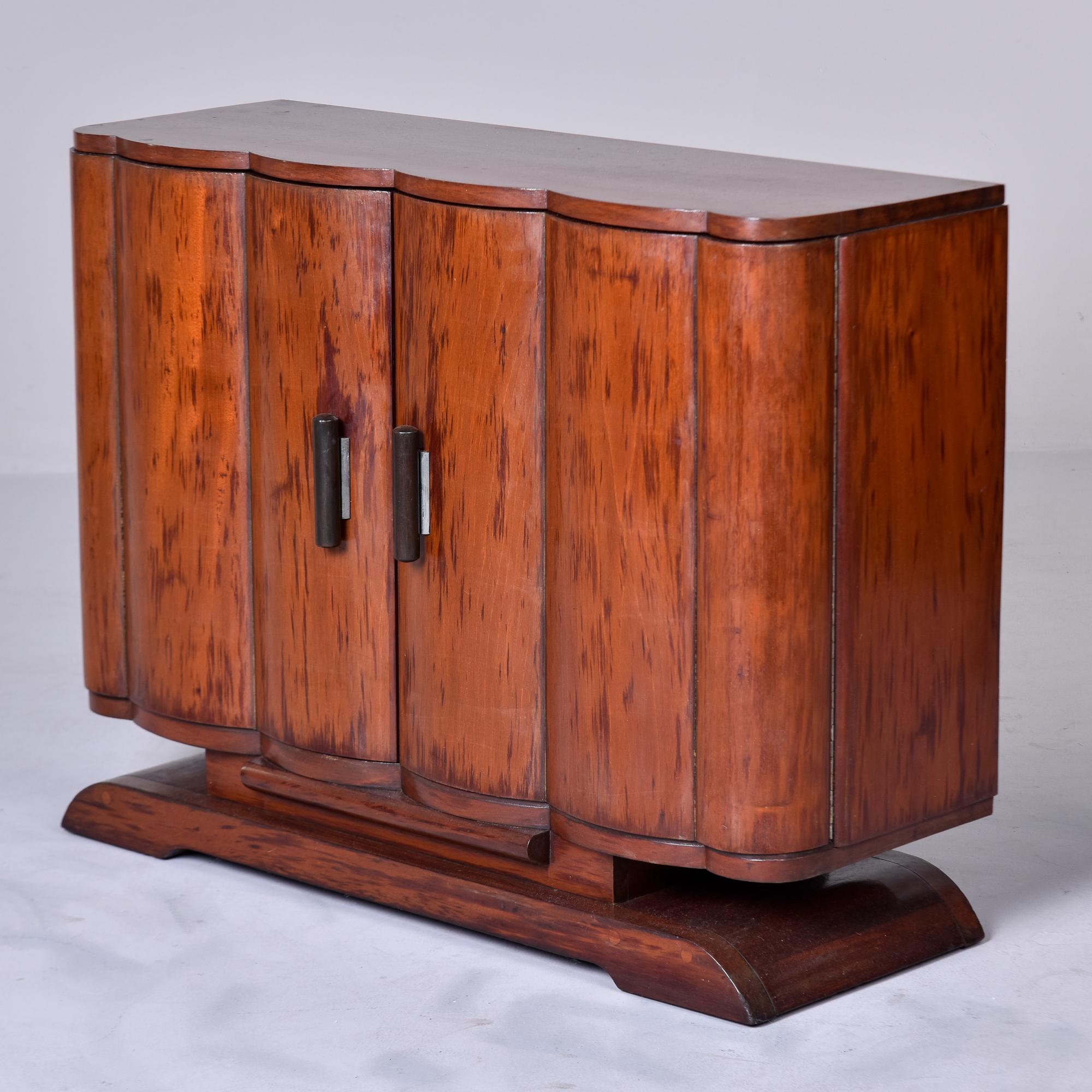 Found in France, this circa 1940s small Art Deco bar or buffet features a curvy pedestal base with a storage compartment. Two doors have curved fronts and open to a compartment with a single, fixed shelf. Previous owner cut out circles from back