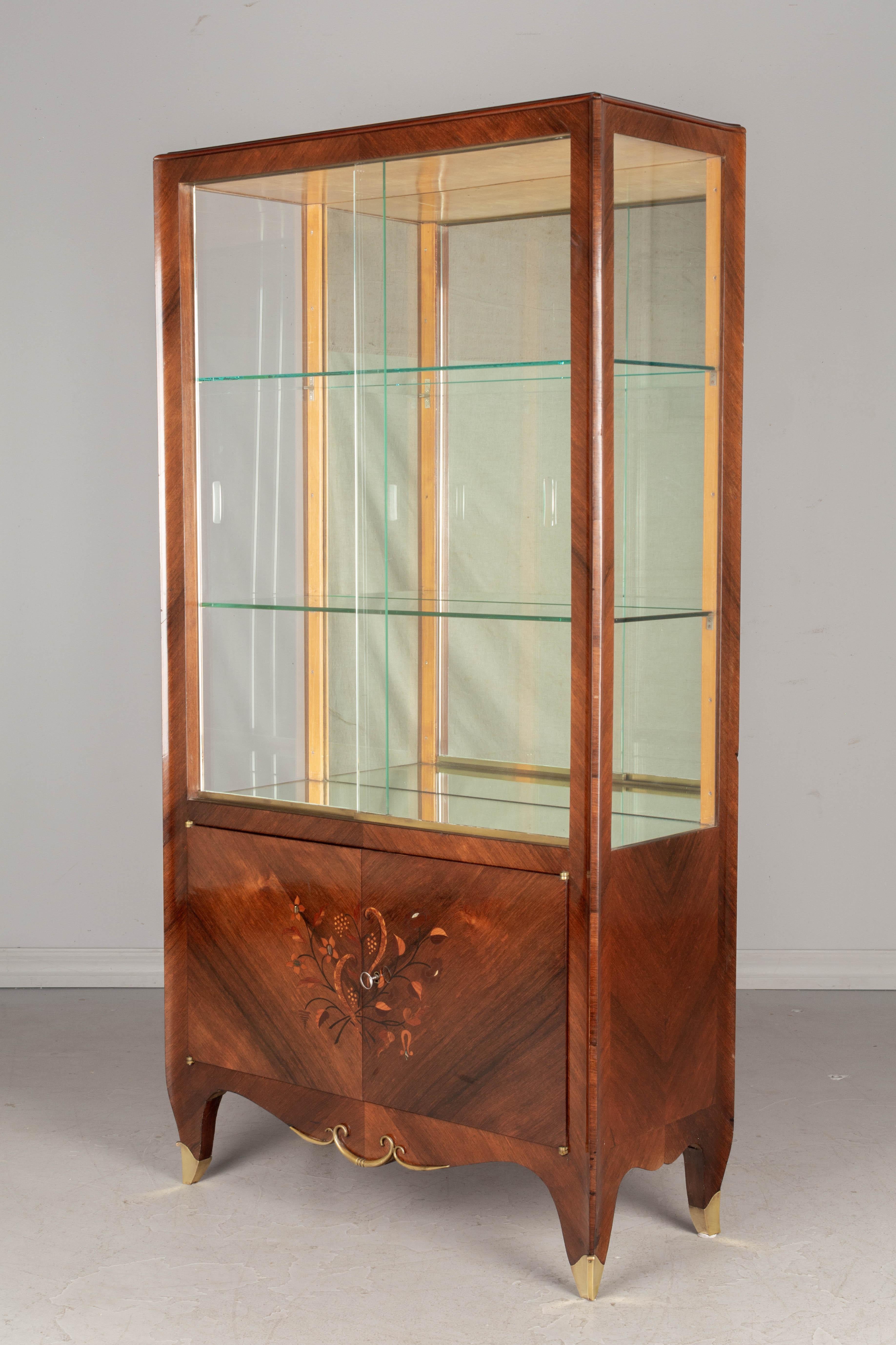 A French Art Deco mahogany marquetry vitrine, or display cabinet, attributed to designer and decorator Baptistin Spade (1891-1969). Fine stylized floral decoration with mother of pearl and abalone inlay. Scalloped apron with brass decoration and