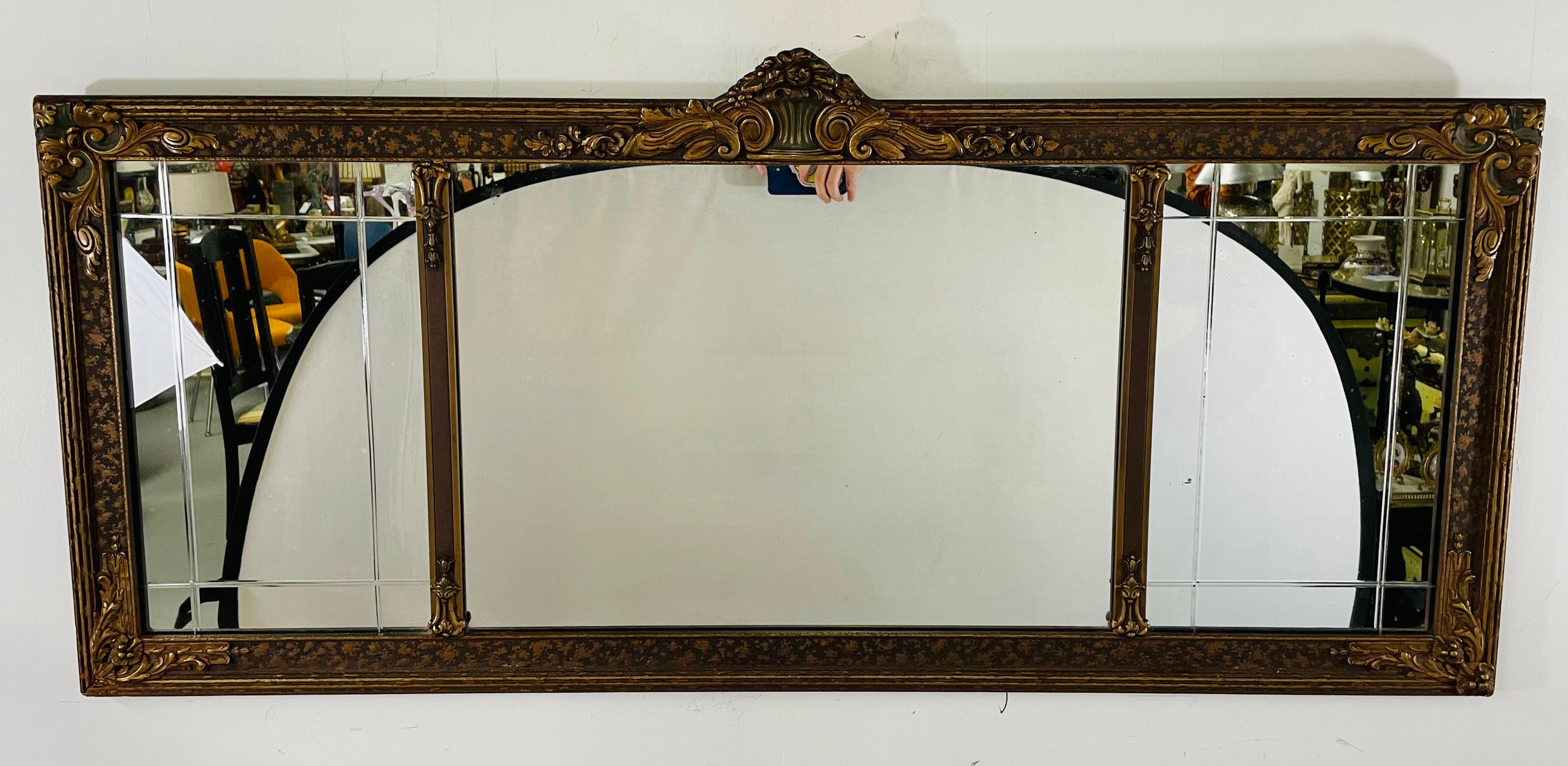 An exceptional French Art Deco three paneled overmantel mirror featuring carved gilt wood and a lovely floral design all over the frame with a carved cartouche in acanthus leaf design. Both side mirror glass panels are decorated with rectangular