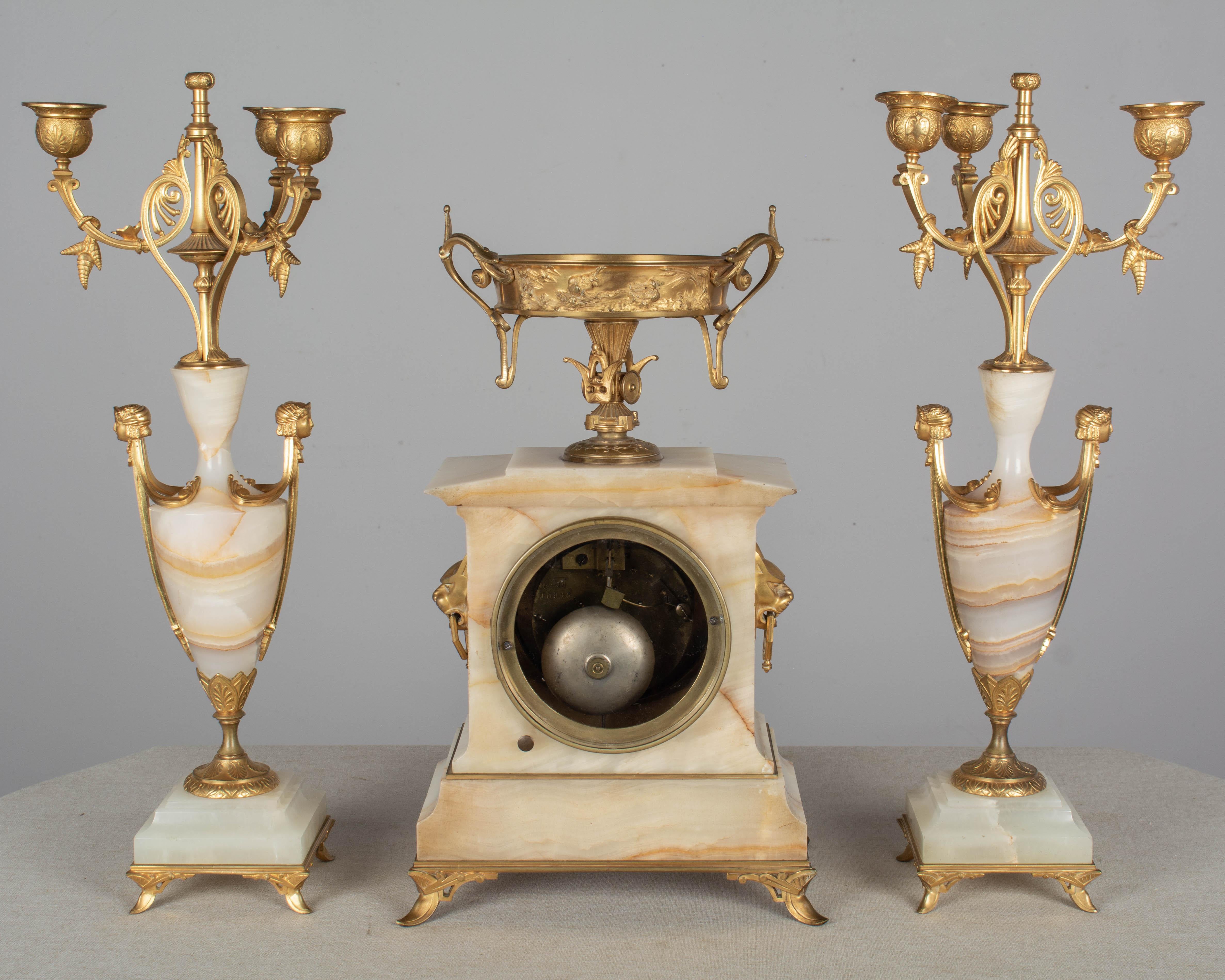 A French Art Deco three-piece mantel garniture consisting of a clock and a pair of three-light candelabras. Onyx and bronze doré with fine casting and bright gilt. Clock face has name of maker: Oudin, Marseille. In working condition and striking on