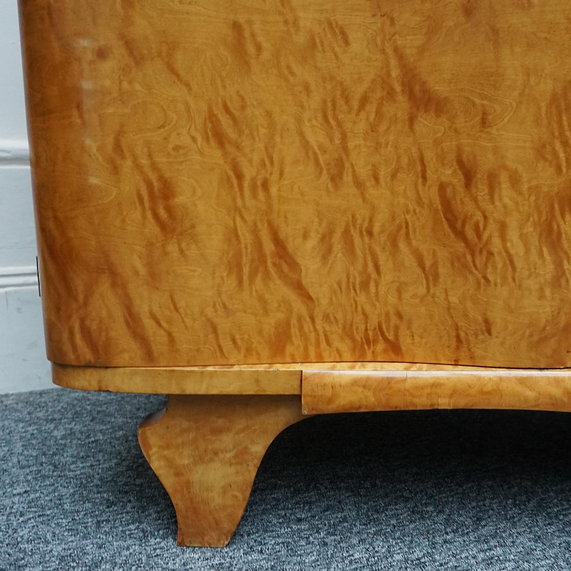 An Art Deco Sideboard. Maple veneered on solid oak with four doors opening to reveal three shelves to either side and single upper left drawer. Original lock and single key.. 
