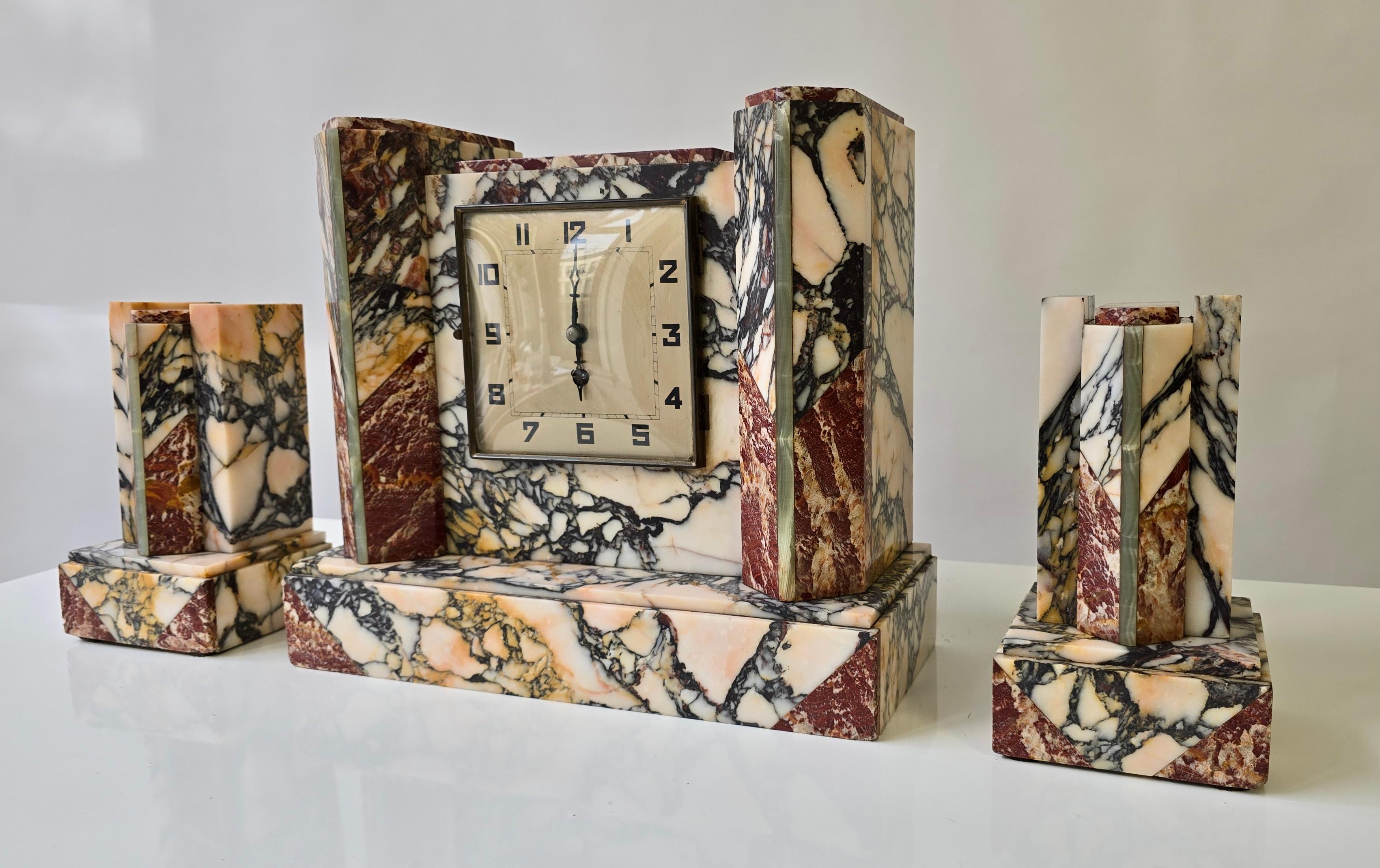 French Art Deco Marble Mantel Clock with Garnitures, UCRA, circa 1930

A striking French Art Deco clock set, circa 1930, comprising a central marble mantel clock and two matching garnitures. The architectural case is crafted from richly colored